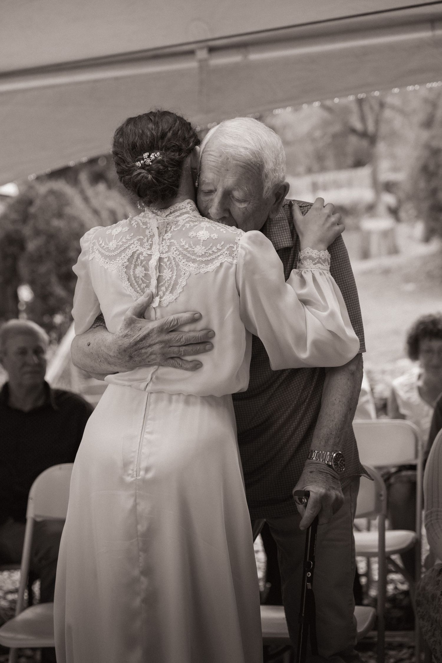 Elderly couple sharing an emotional dance at a wedding, bride in white lace gown, black and white photo.