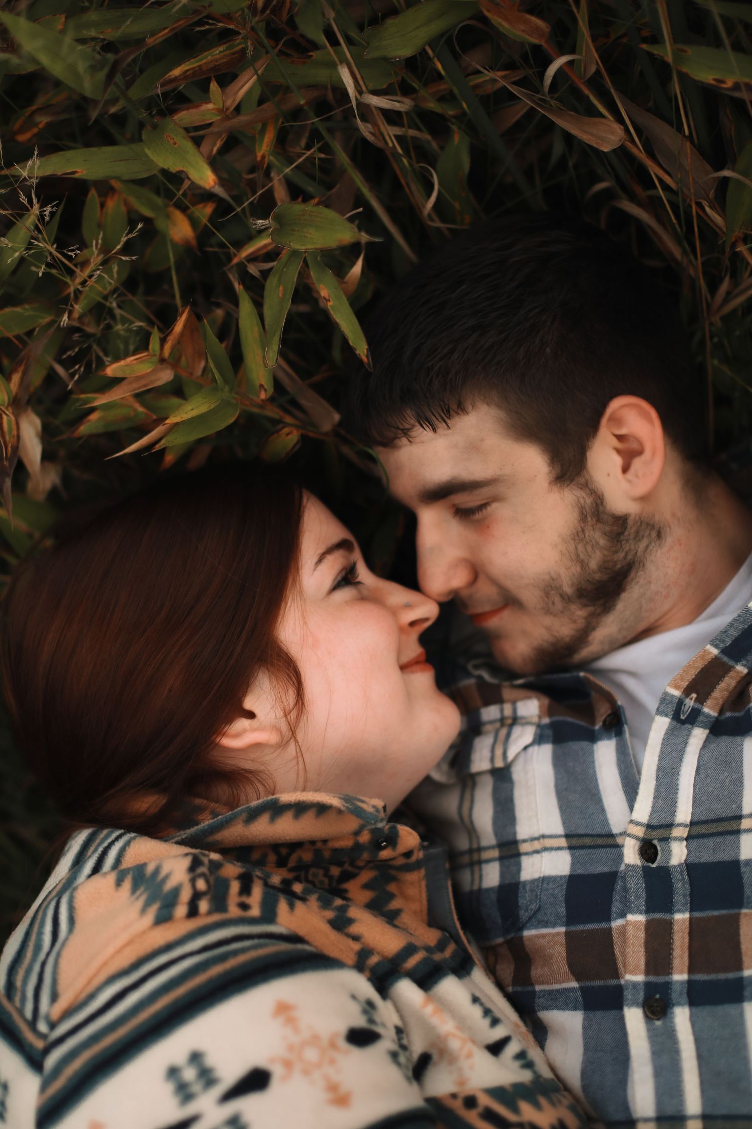 A romantic couple embraces intimately against a backdrop of eucalyptus leaves at sunset.