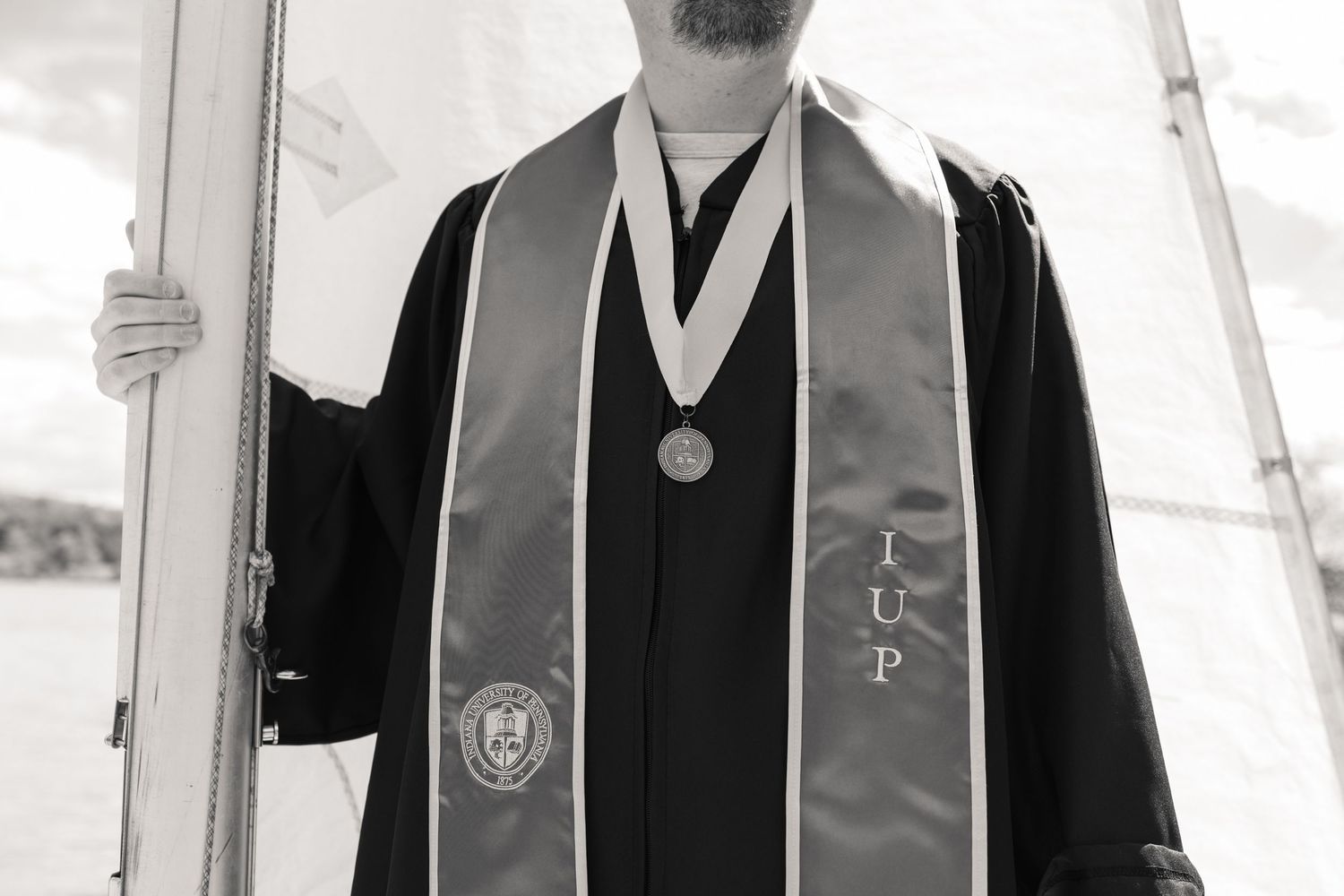 Graduate in black robe with IUP stole and medal poses at Indiana University of Pennsylvania commencement ceremony.