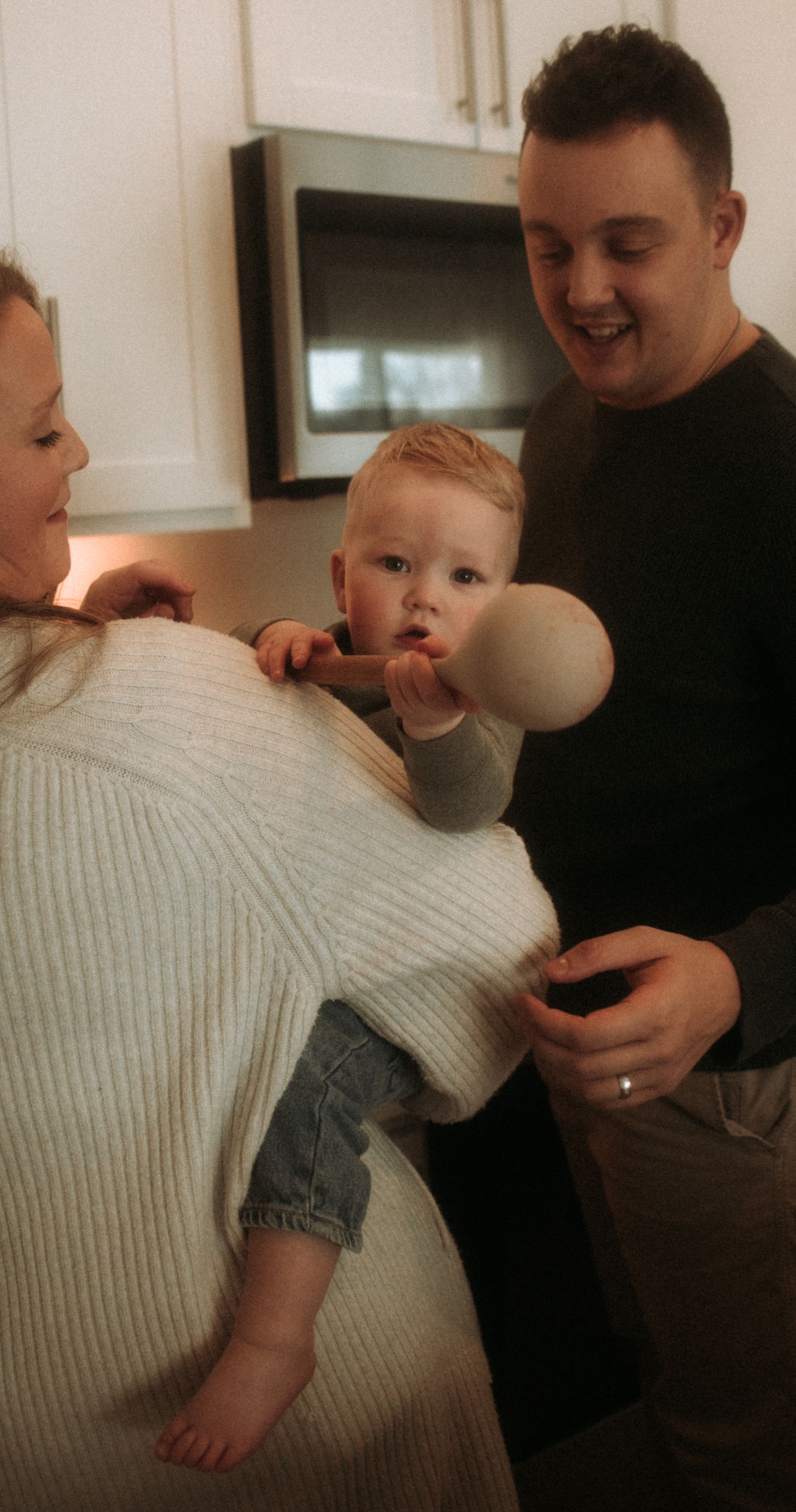 A sequence of playful moments shows a baby in denim shorts being lifted and swung by someone wearing a white sweater.