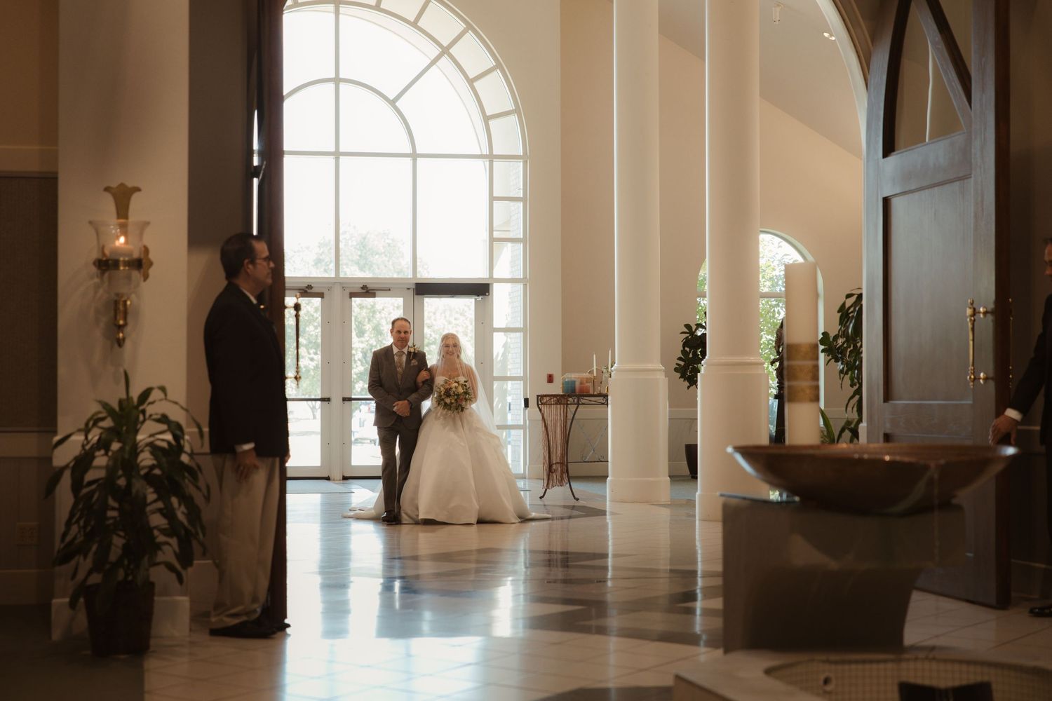 Bride and groom share a romantic moment in an elegant wedding venue lobby with arched windows and marble floors.