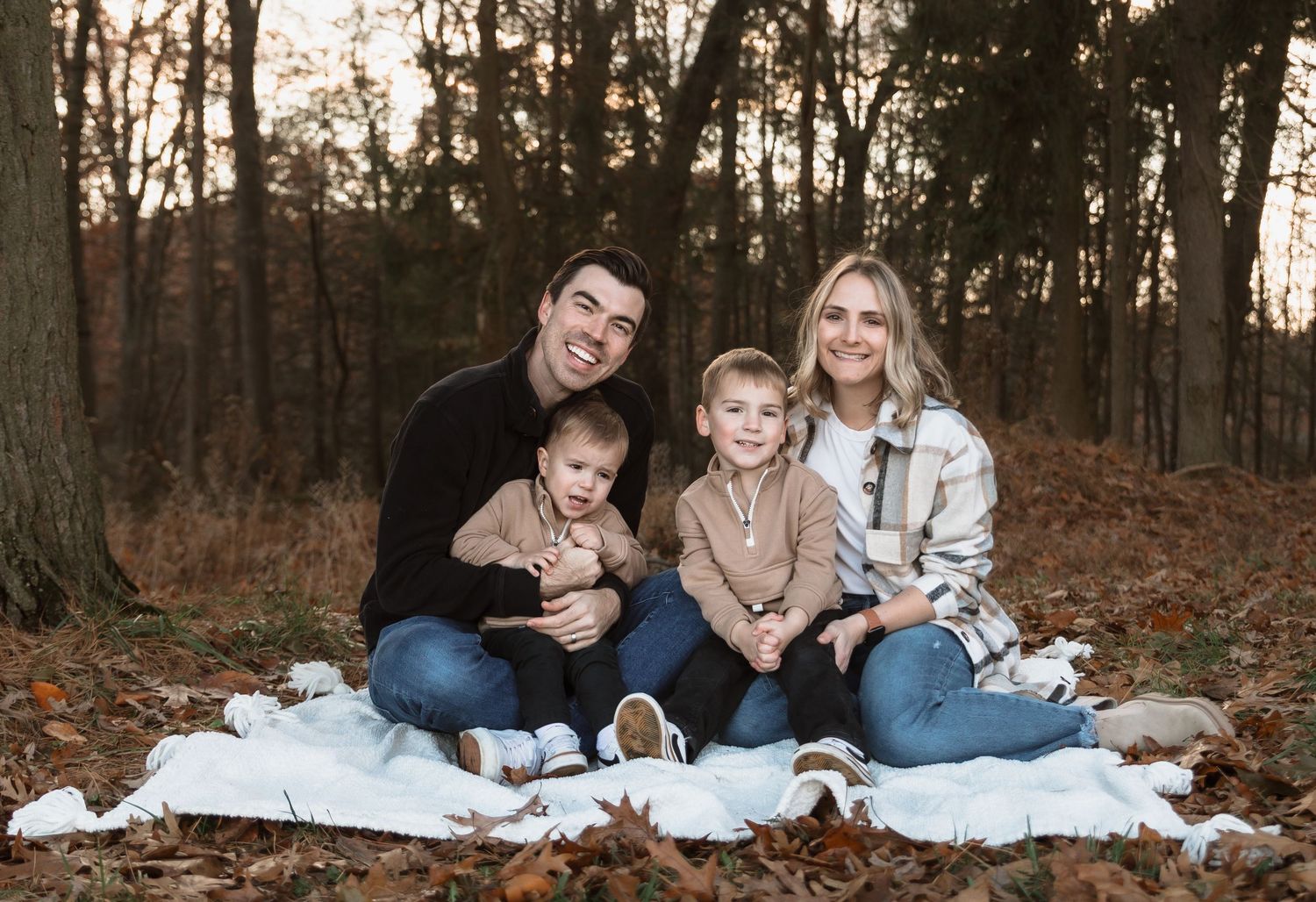 Family wearing coordinated blue and white outfits poses together on autumn leaves in a wooded setting.