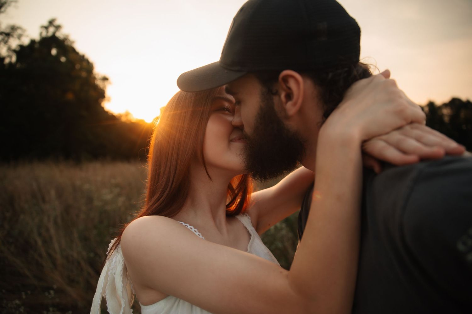 A couple shares a romantic kiss during sunset in a golden-lit outdoor setting.