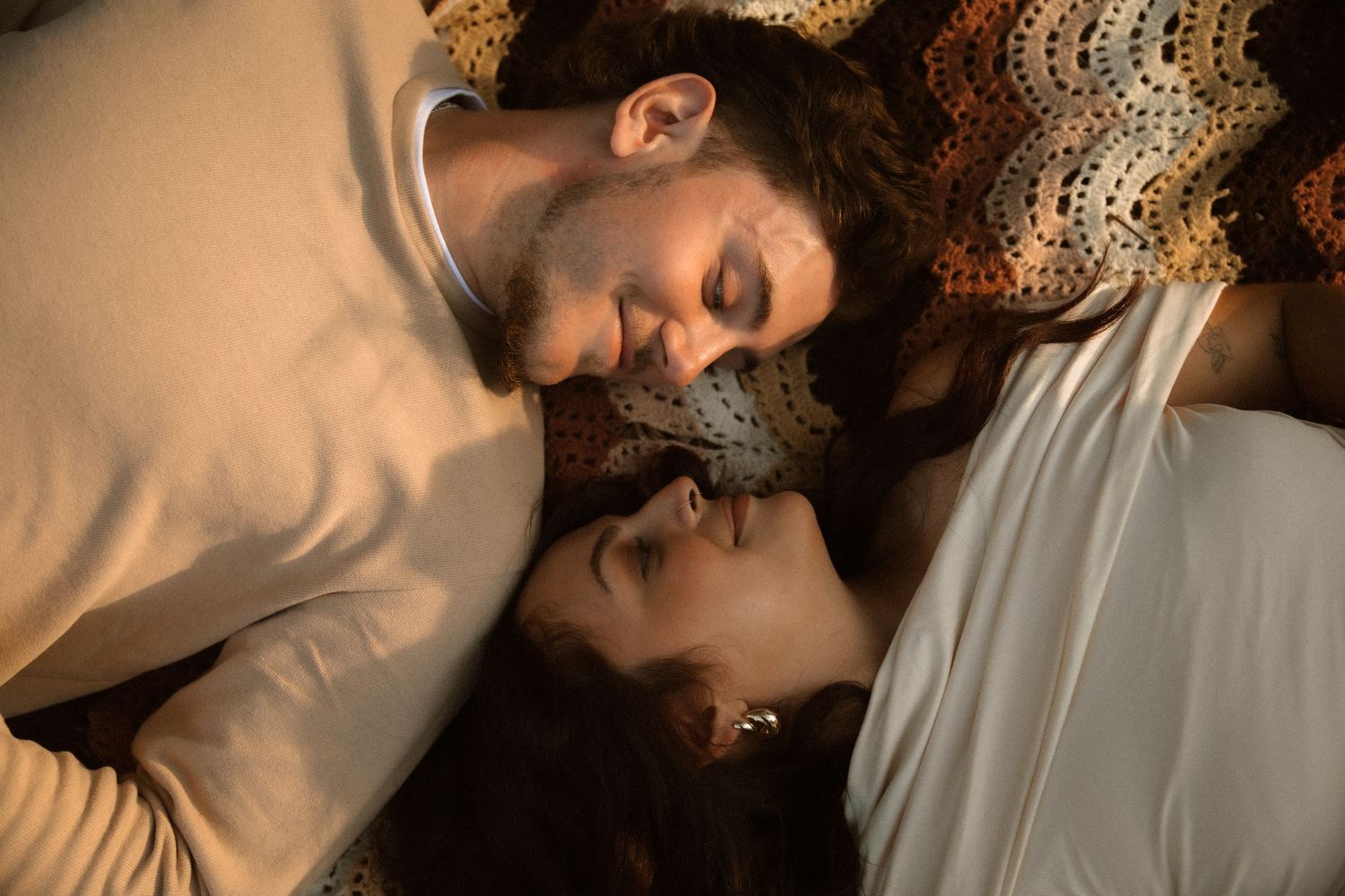 Two people lying down with heads close together on a patterned surface in warm lighting.