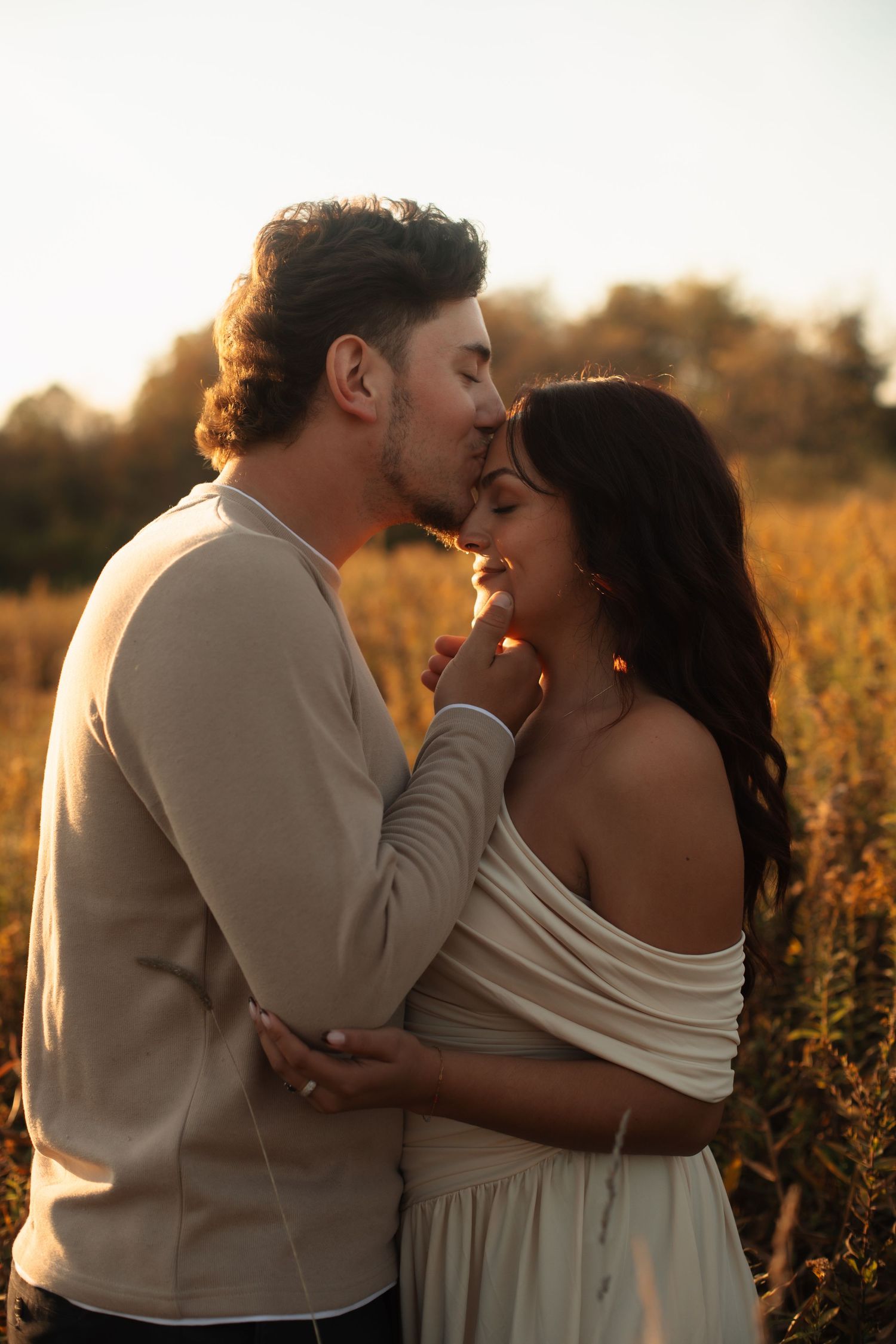 A couple shares romantic kisses in a golden field at sunset during their wedding photoshoot.