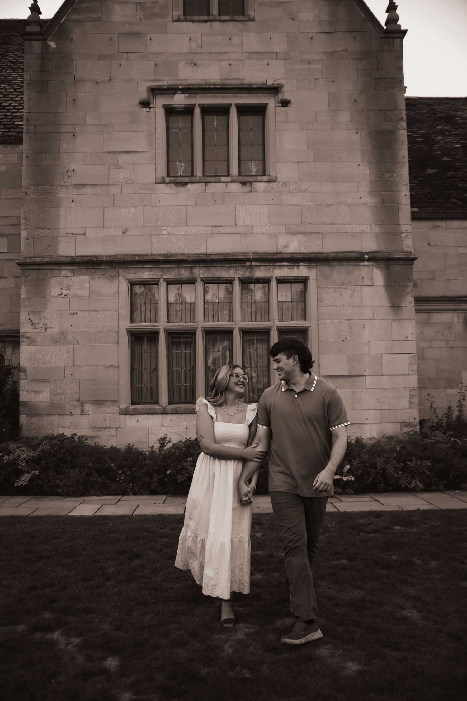 A couple playfully interacts in front of a stone building in a romantic black and white photo series.