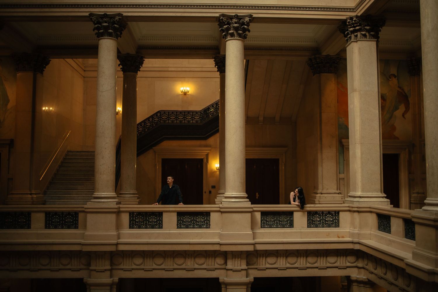 Grand neoclassical interior with tall Corinthian columns, ornate balcony, and elegant staircase in a historic government building.