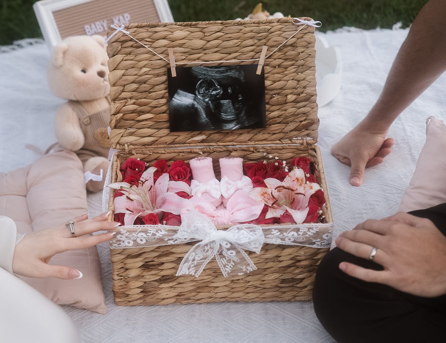 Wicker basket with baby ultrasound photo, pink roses, orchids, and bow for gender reveal or baby shower gift.