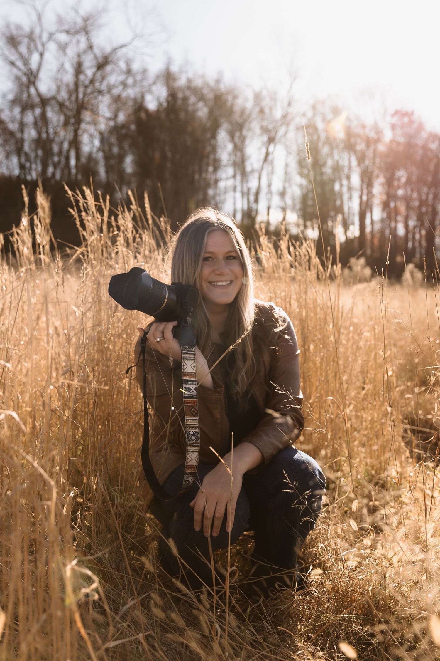Person in black leather jacket poses playfully in golden autumn field during sunset.