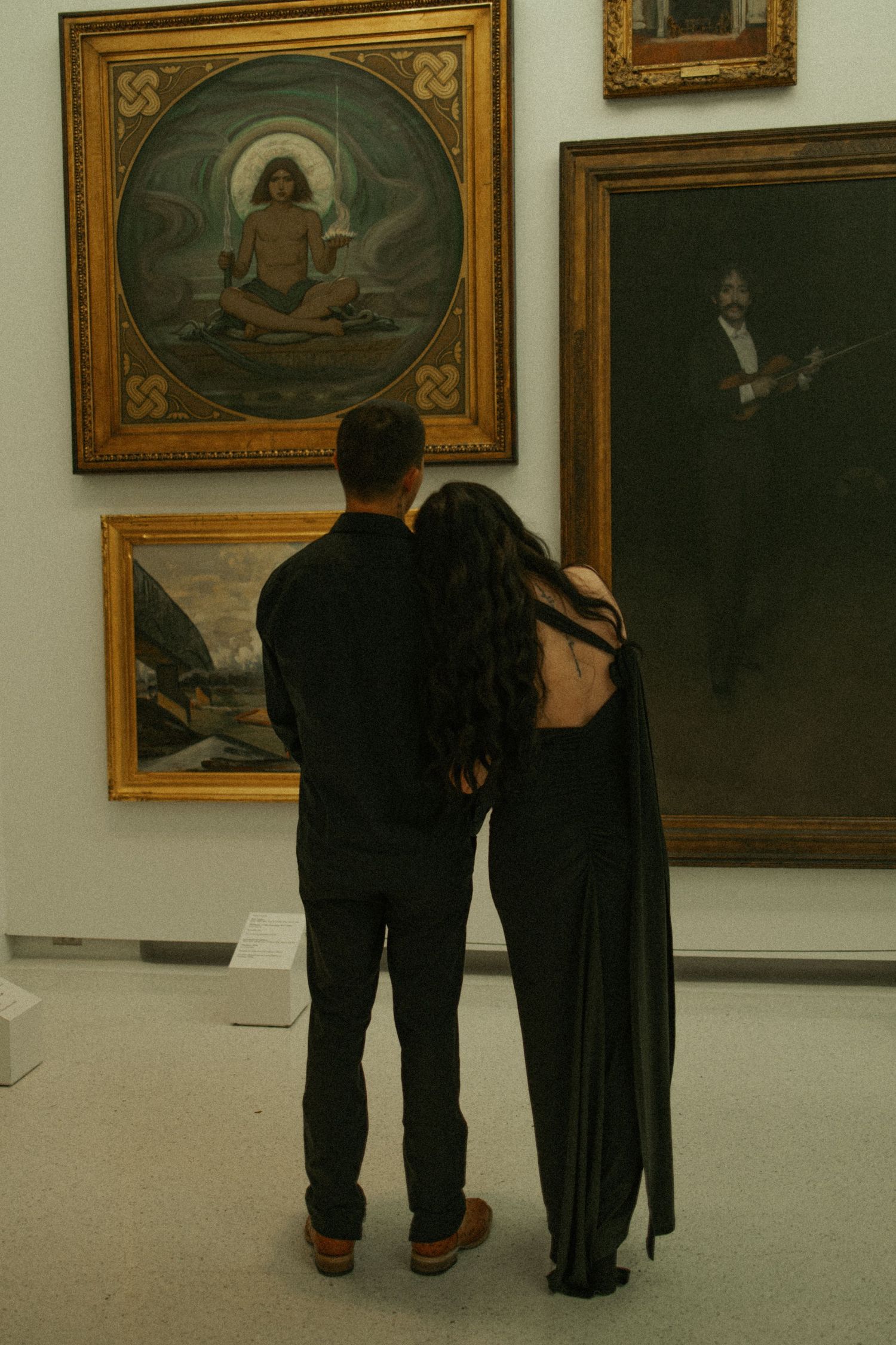 Couple in black attire viewing classical paintings in an art gallery museum.