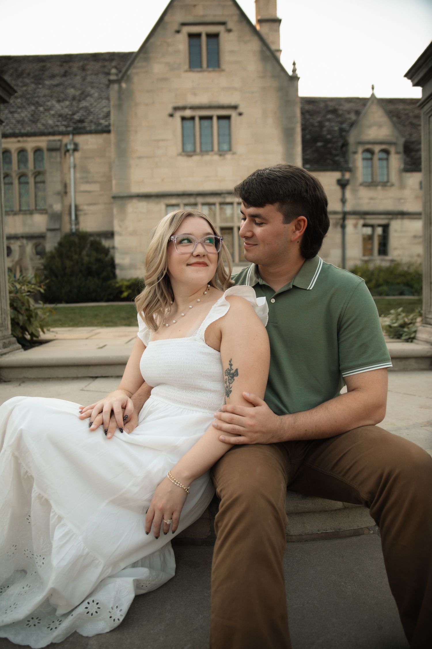 A couple sits together on a stone bench outside a historic stone building.