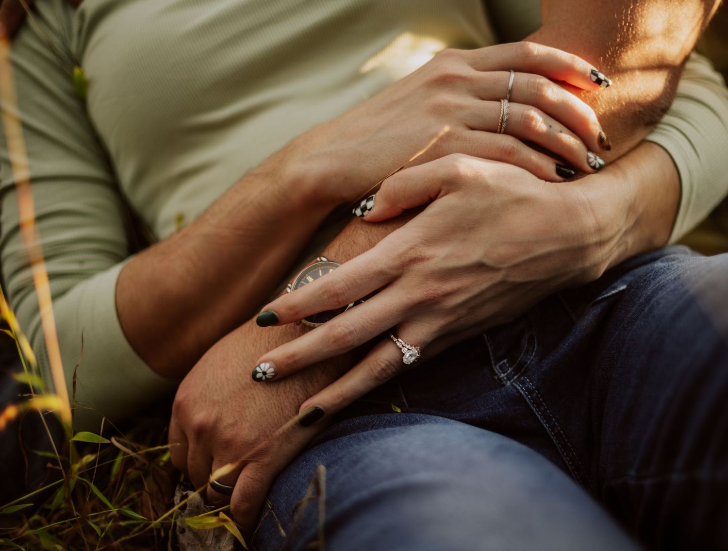 Close-up view of hands with engagement rings against a dark background in natural lighting.