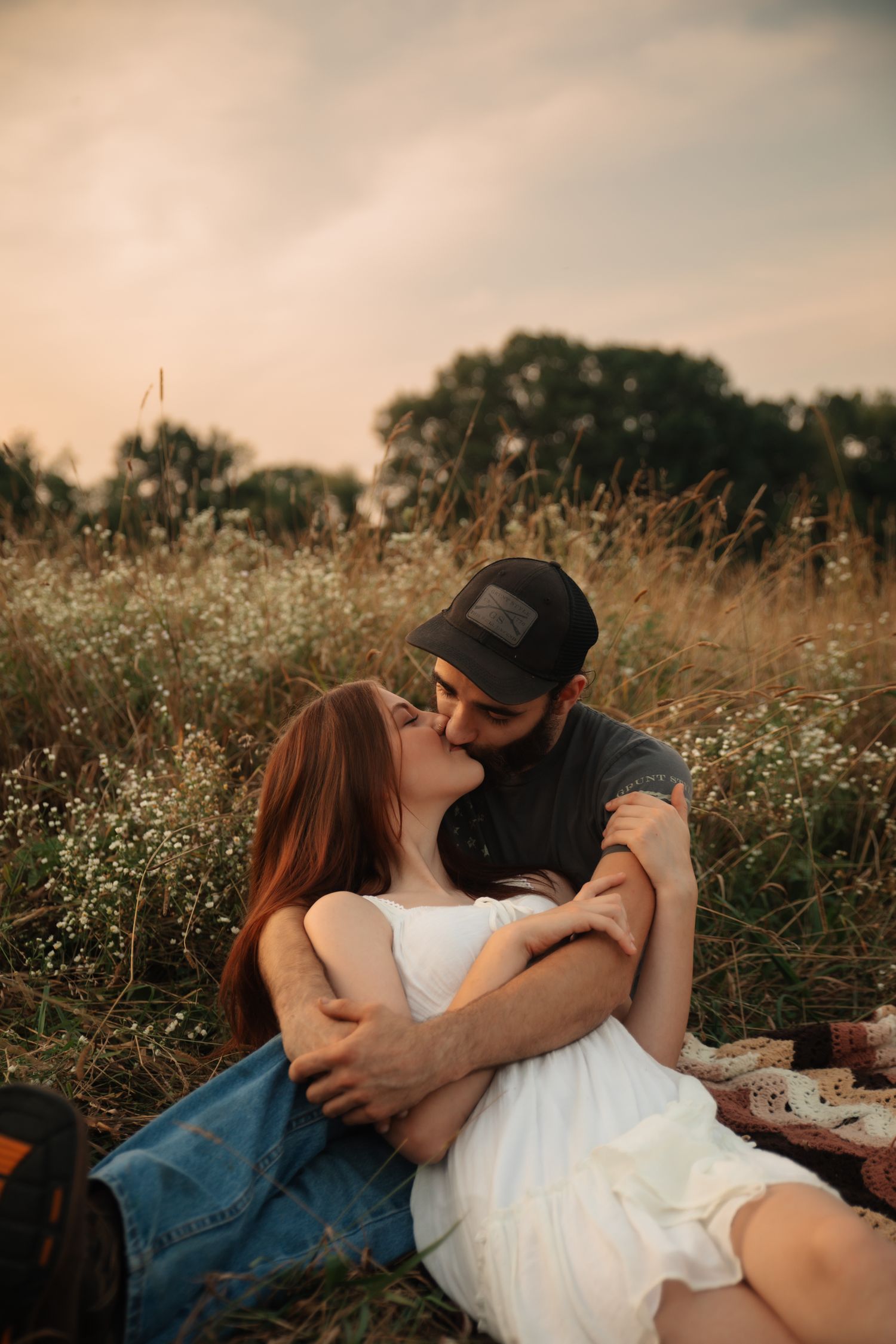 A romantic sunset picnic scene in a wildflower meadow with a couple embracing on a warm summer evening.