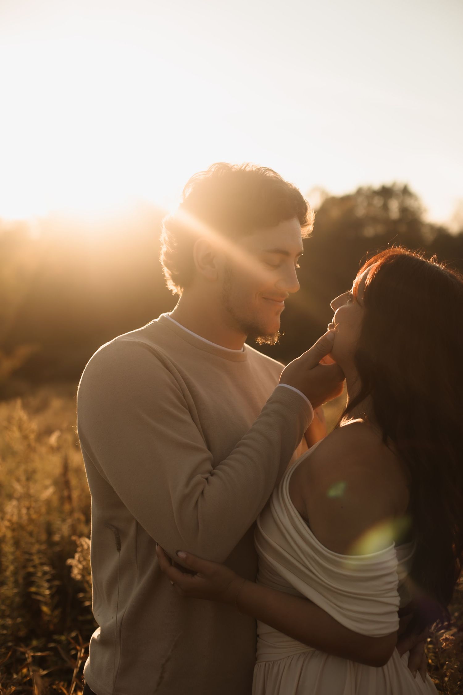 Romantic couple embraces in golden sunlit field during sunset creating a dreamy silhouette.