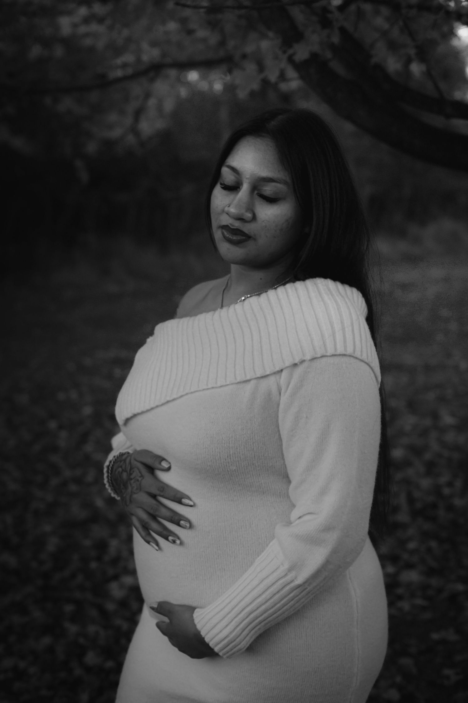 Black and white maternity photos showing pregnant woman in white sweater cradling baby bump in outdoor setting.