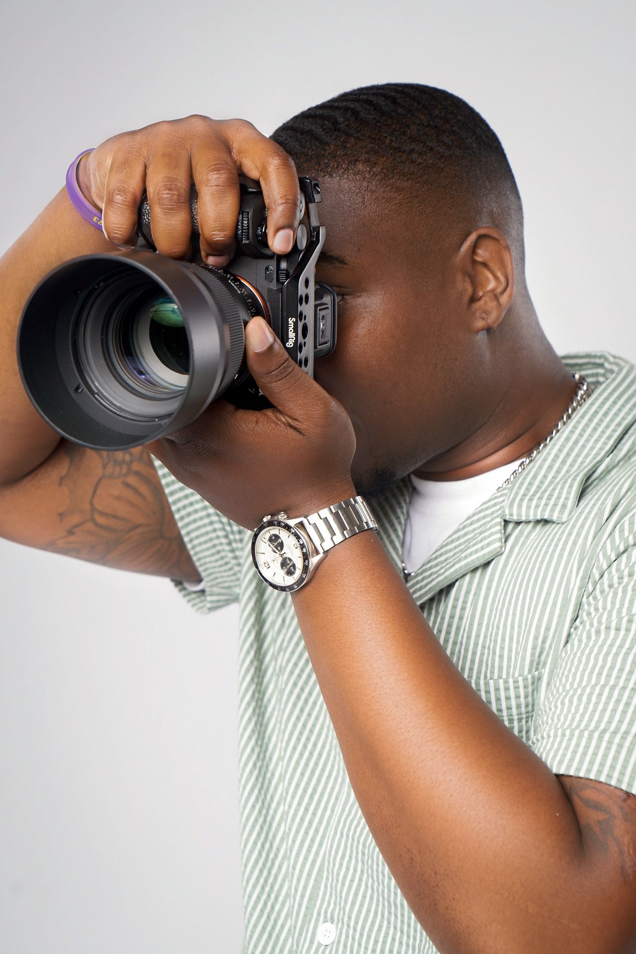 Person in striped shirt photographing with professional camera lens against white background.