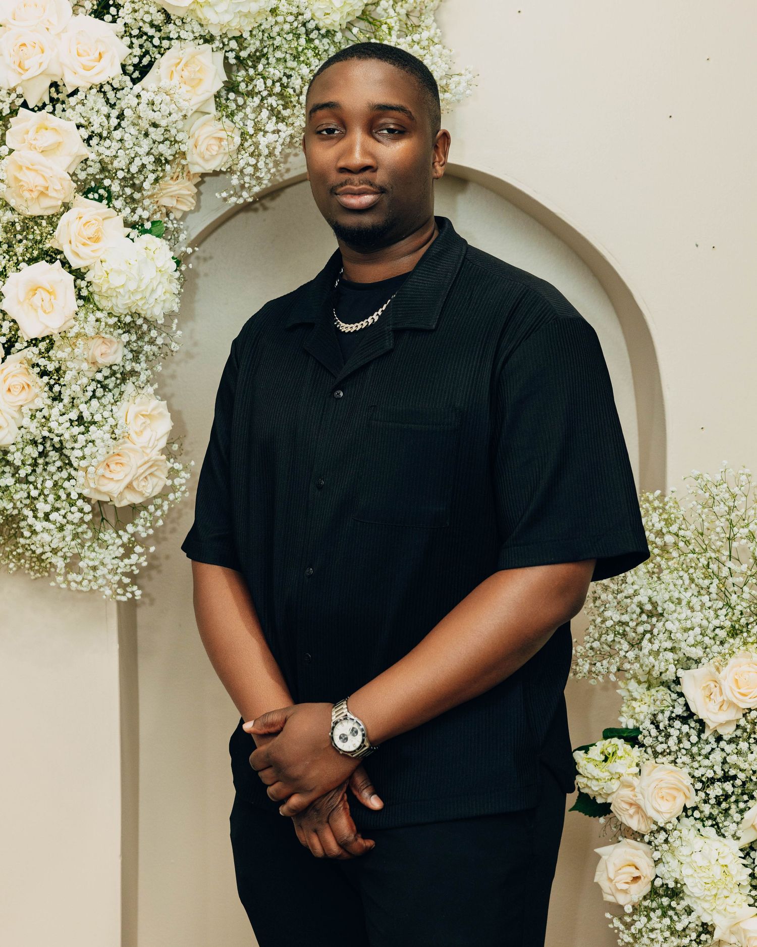 Portrait session in black polo shirt with floral arch backdrop.