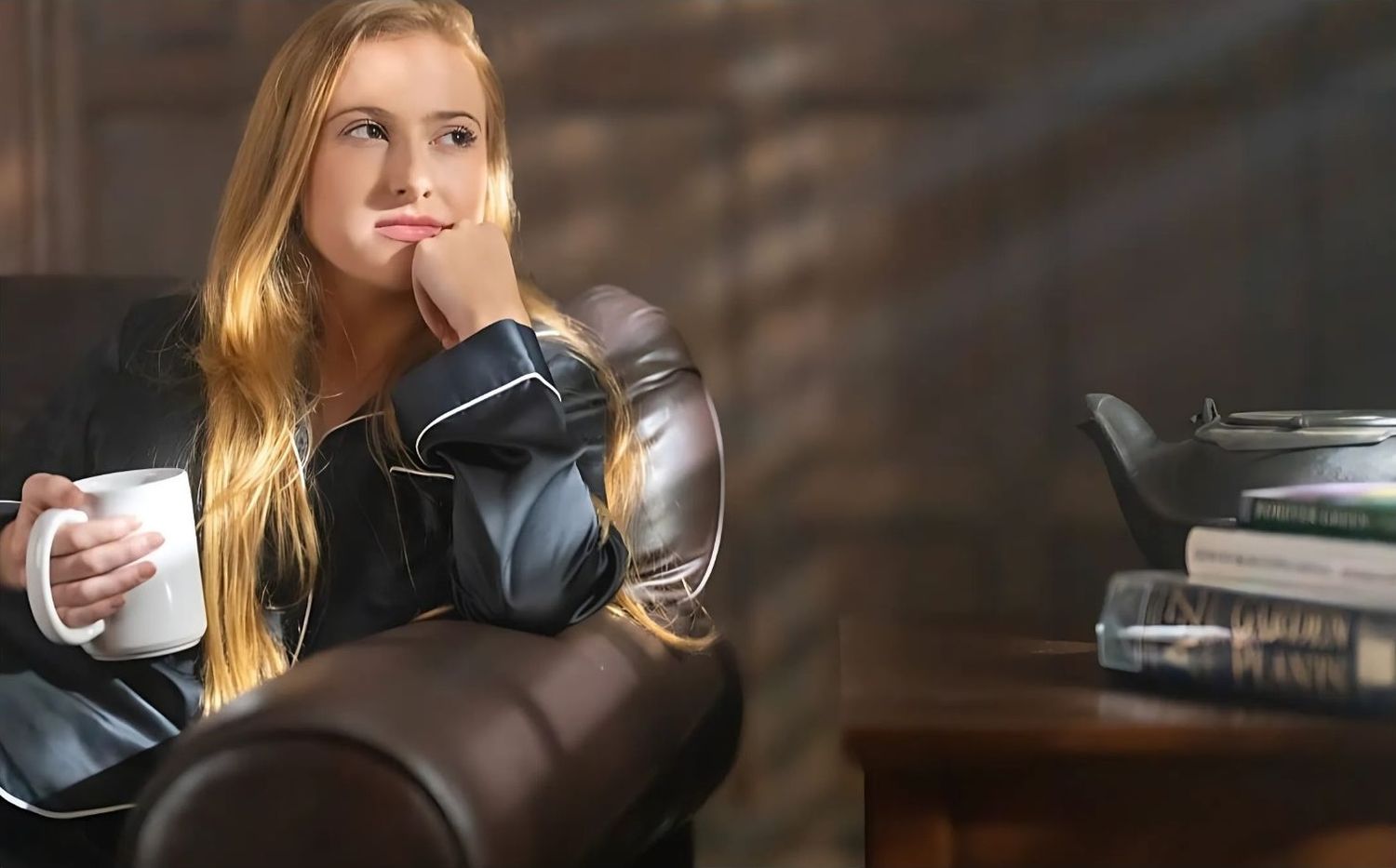 Person relaxing on dark leather couch in moody interior setting.