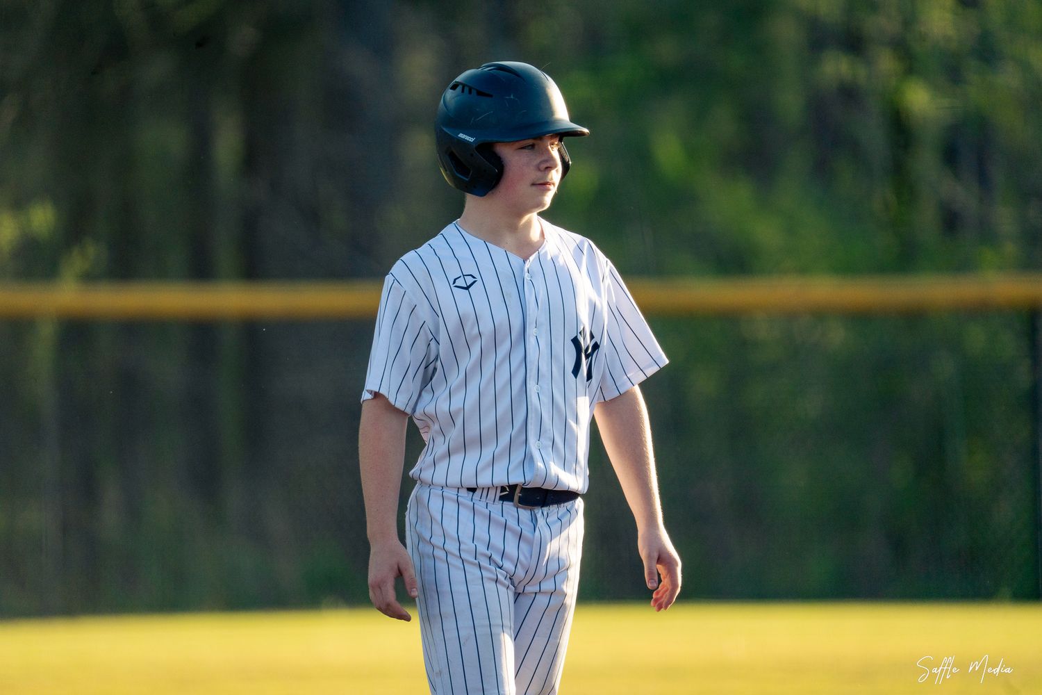 Young baseball player in Yankees pinstripe uniform and helmet standing on base during a game.