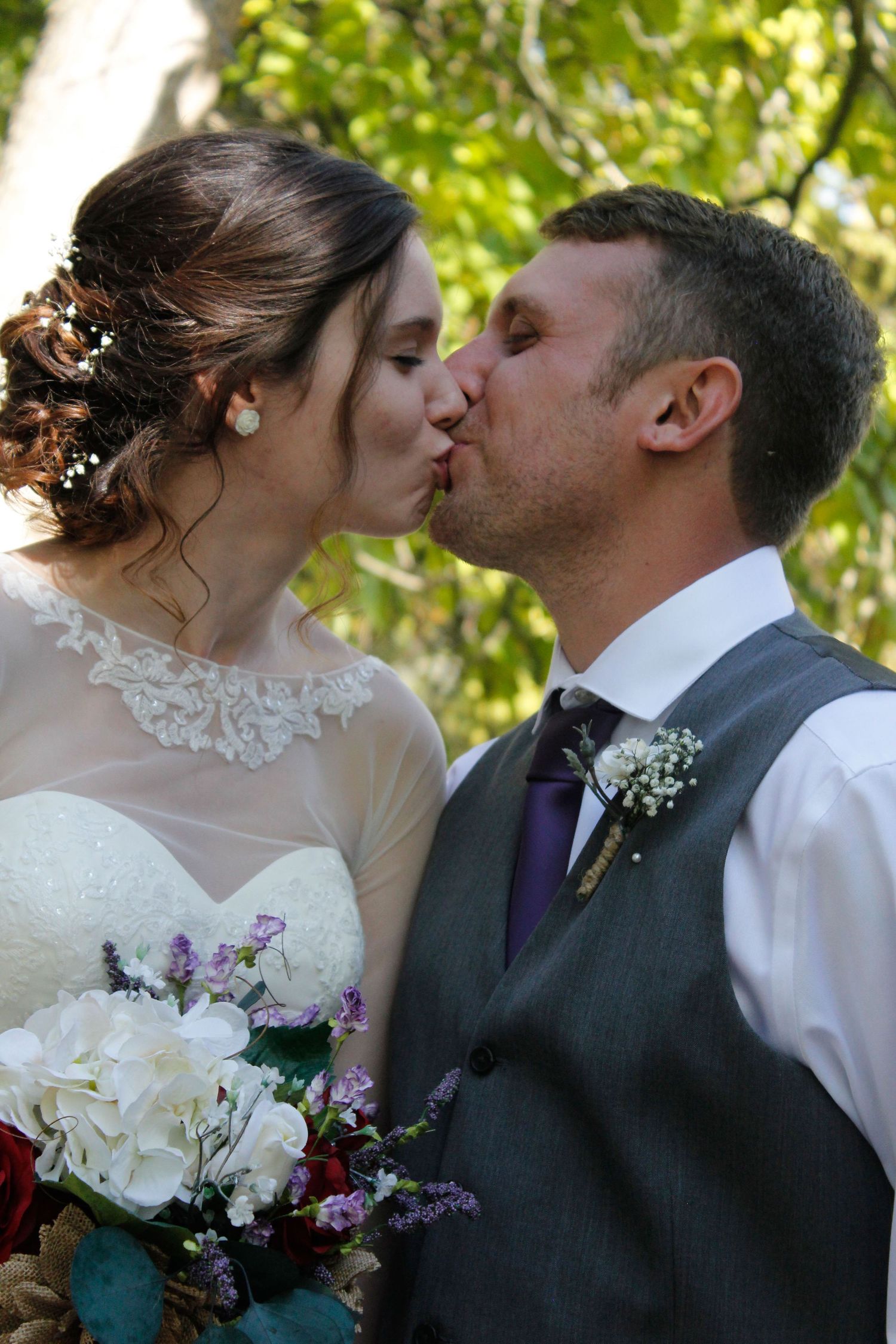 A romantic wedding day kiss shared against a backdrop of green foliage.