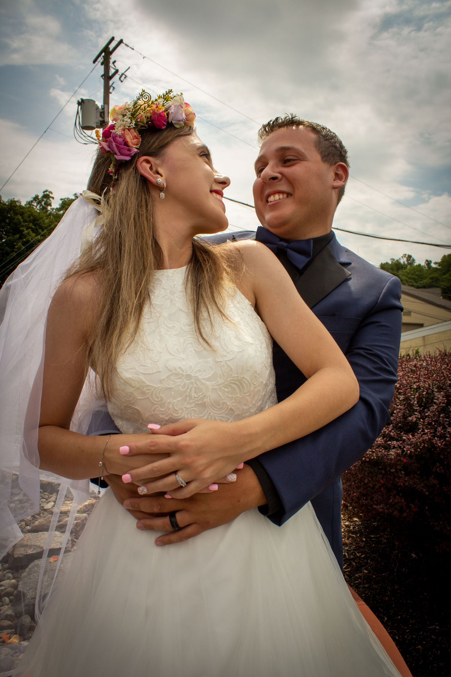 A romantic wedding photo of a couple embracing outdoors, with the bride wearing a floral crown and white dress.