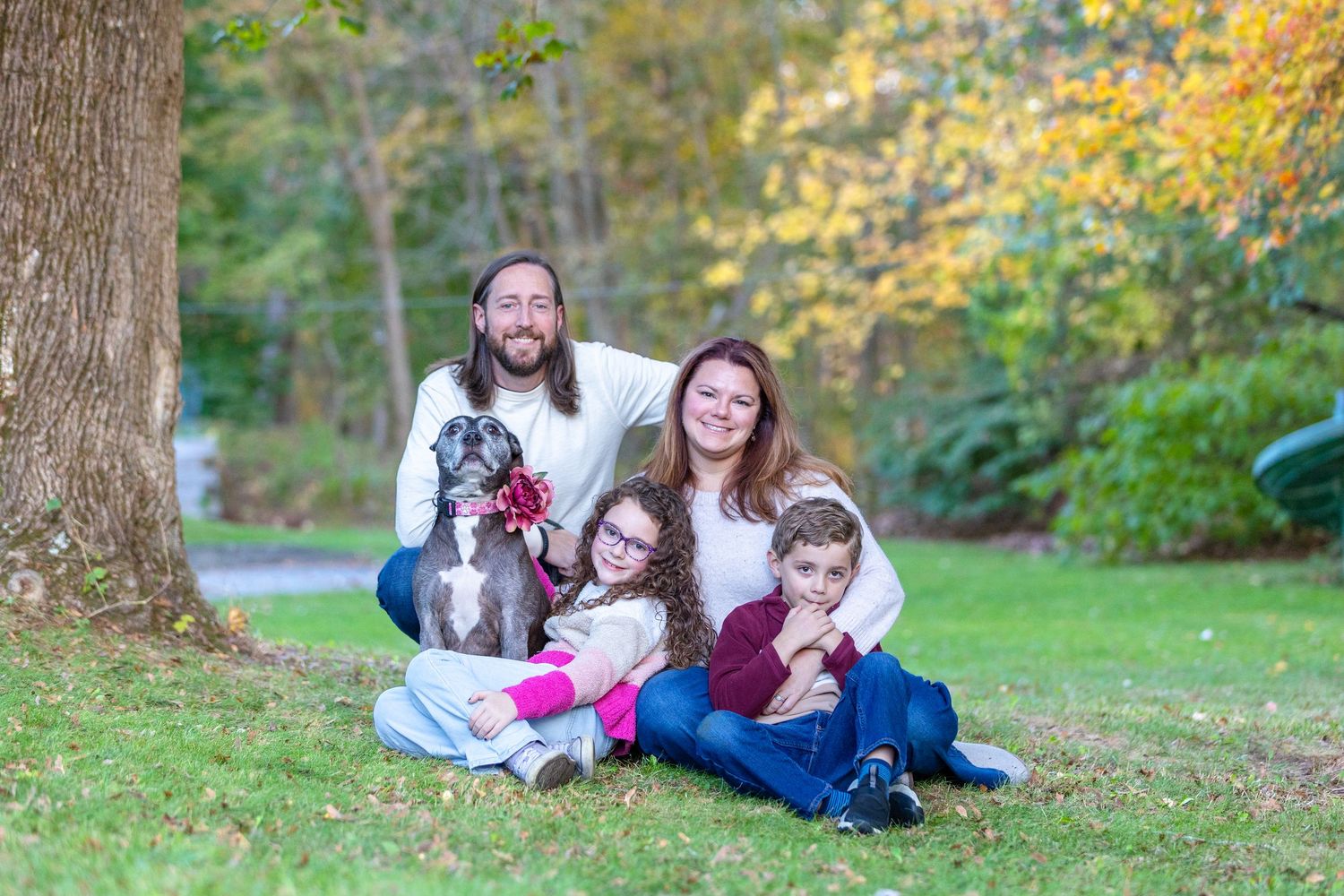 A family lying together on autumn grass surrounded by fallen leaves in a park setting during a photo session.