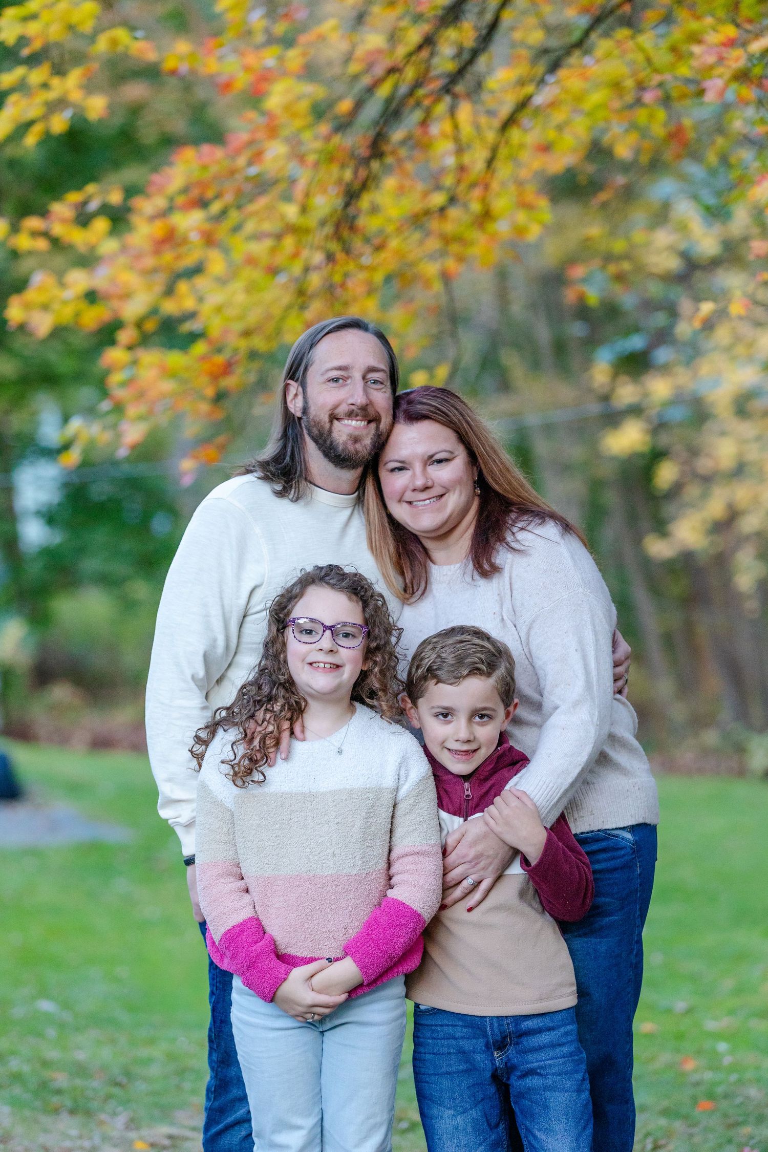 A family shares warm embraces and laughter while posing together against a backdrop of autumn foliage.