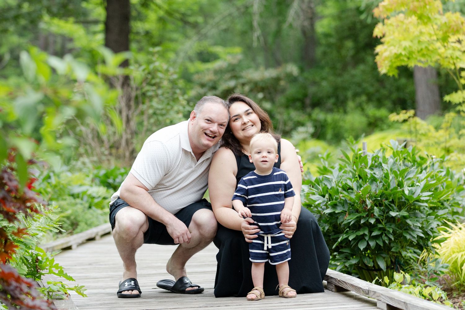 Family enjoying a summer day together on a garden path surrounded by lush green foliage and yellow flowers.