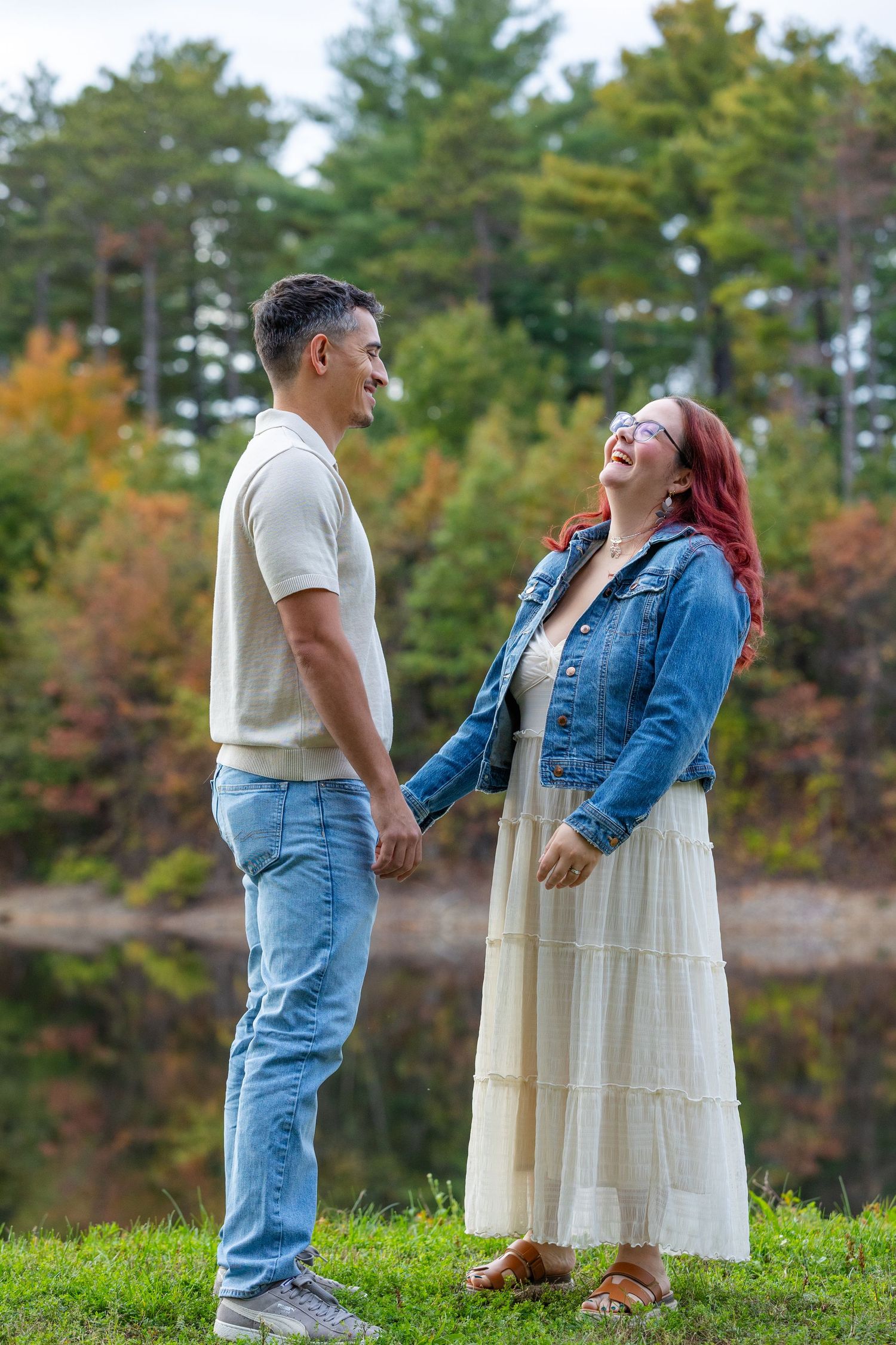 Two people share a joyful moment together outdoors on grassy hill with autumn trees in background.