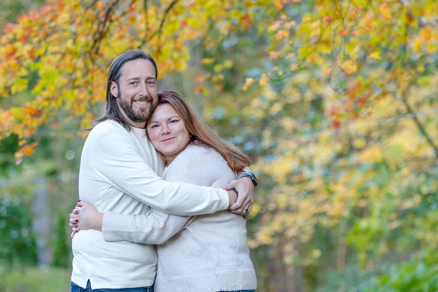 A couple embraces outdoors during autumn with golden leaves in the background.