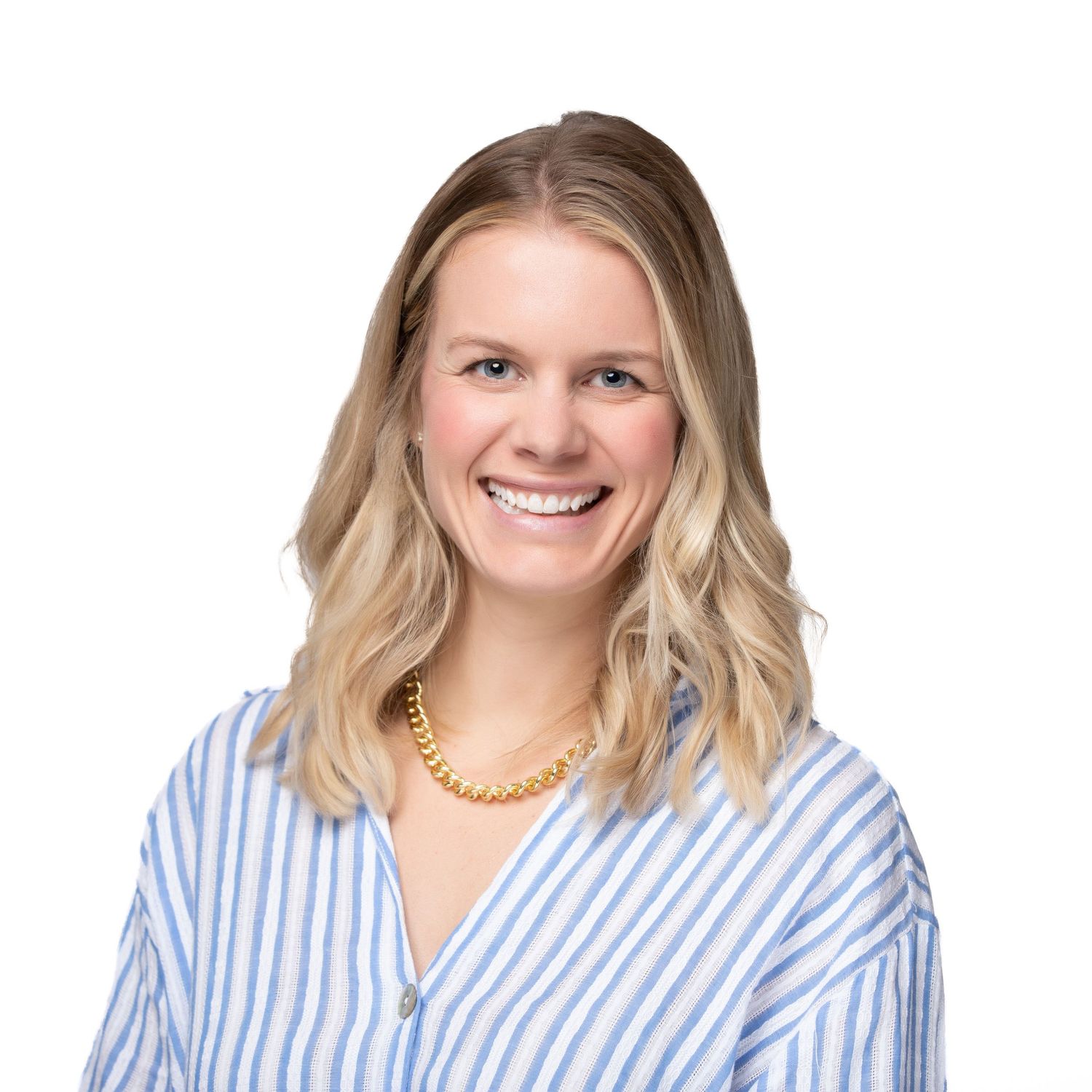 Smiling blonde woman in a blue striped shirt and gold necklace poses for a professional headshot photo.