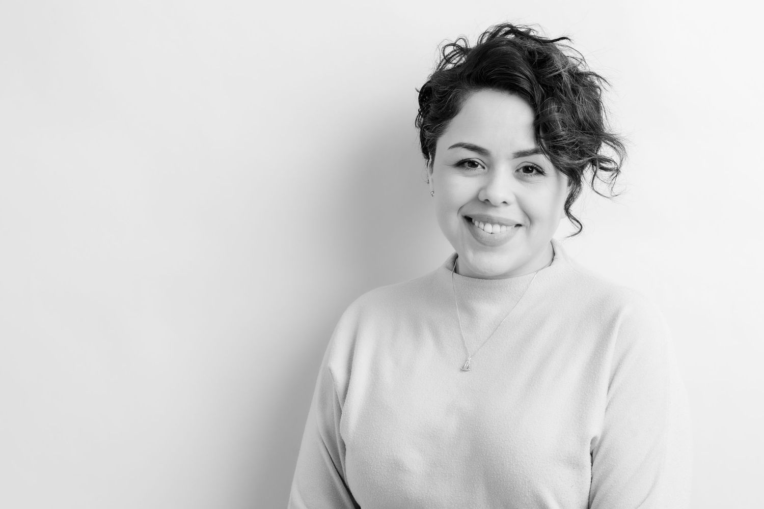 Black and white portrait of a smiling young woman with curly hair wearing a light sweater against a white background.