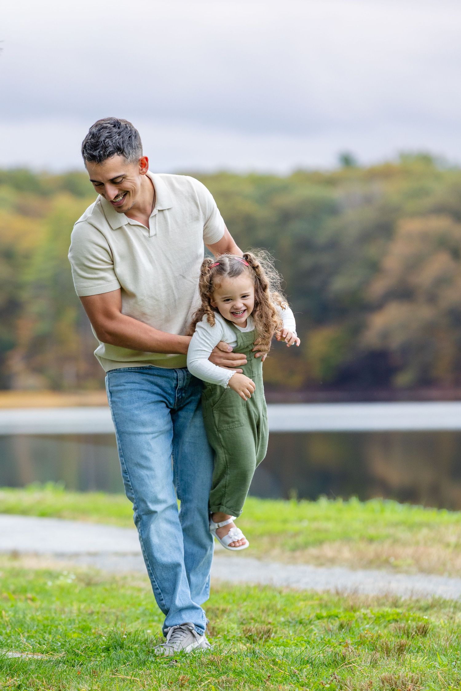 A parent and child play together on a grassy hillside overlooking a lake on a sunny autumn day.
