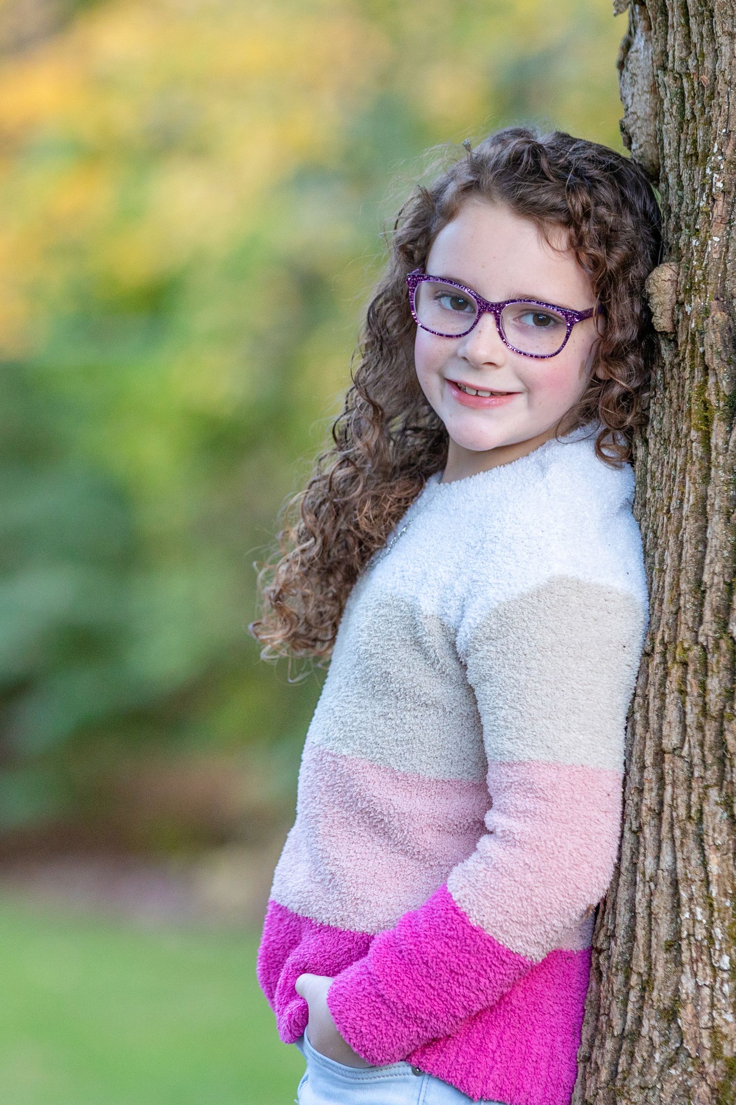 A series of outdoor portrait photos showing someone in a color block sweater leaning against a tree in natural lighting.