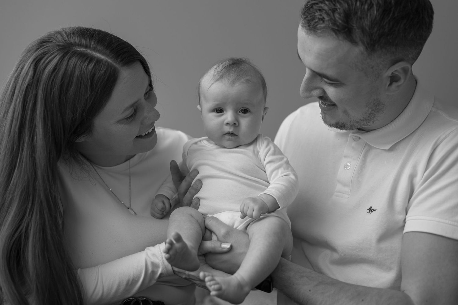 Newborn baby lying on bed surrounded by family during lifestyle photography West Yorkshire
