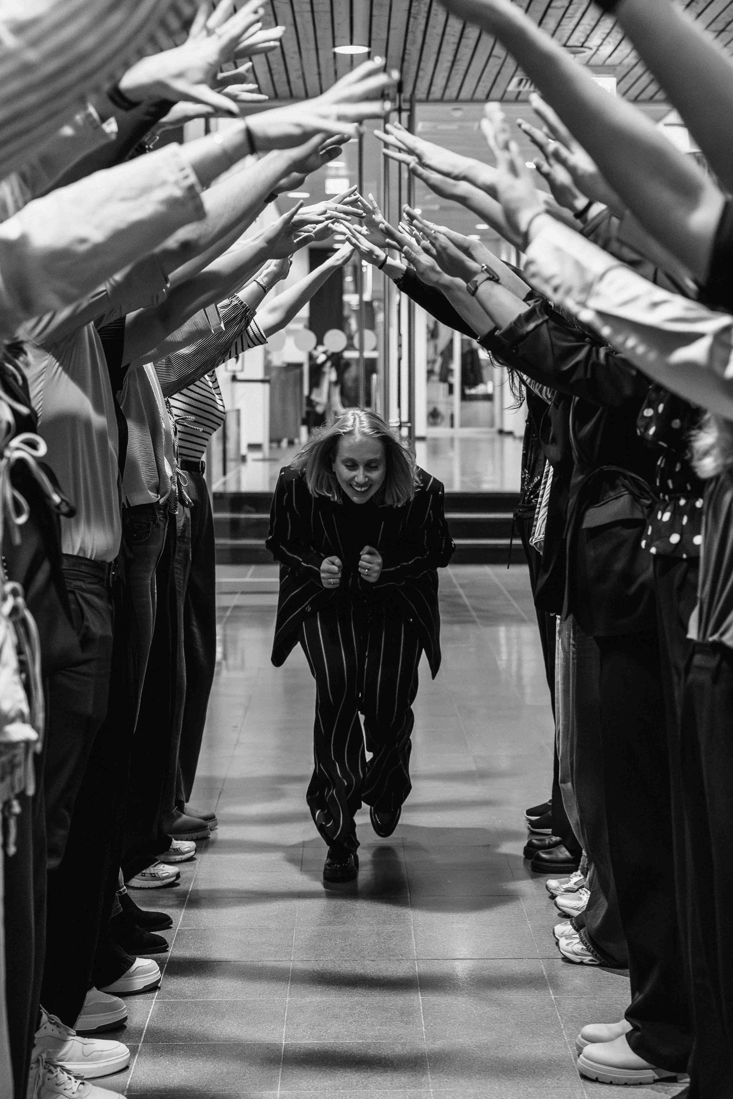 Black and white photo of a woman walking through a tunnel of raised hands formed by two rows of people.