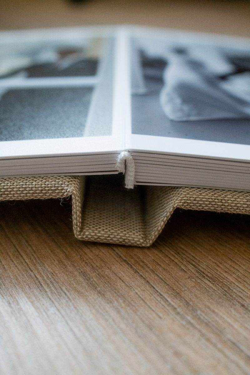 Open photo album with burlap cover lying flat on wooden table, showing black and white wedding photos inside.