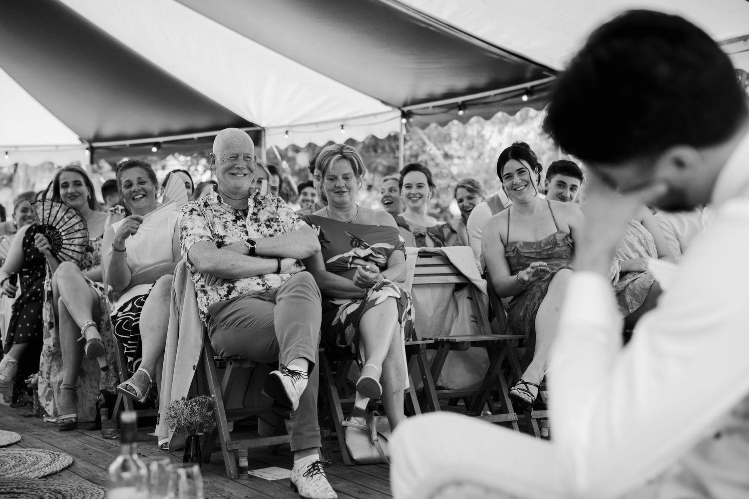 Guests seated under a tent watching a wedding ceremony in black and white photography.