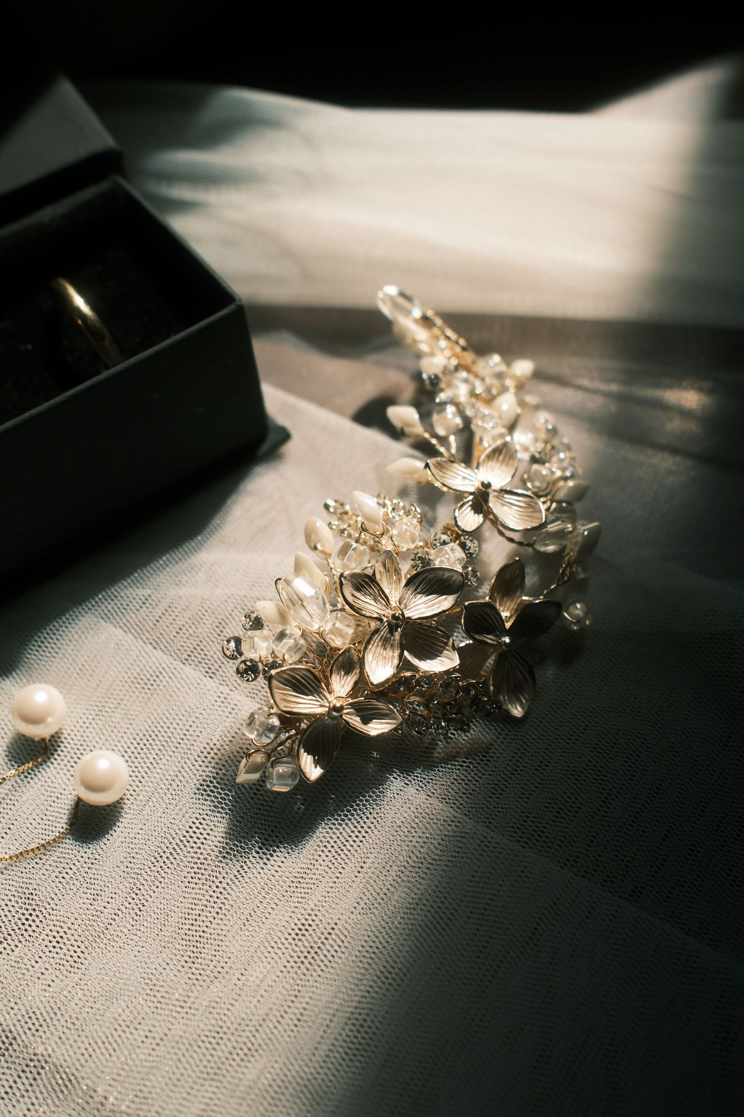 Elegant gold floral bridal hair comb with crystals and pearl earrings on white tulle fabric.