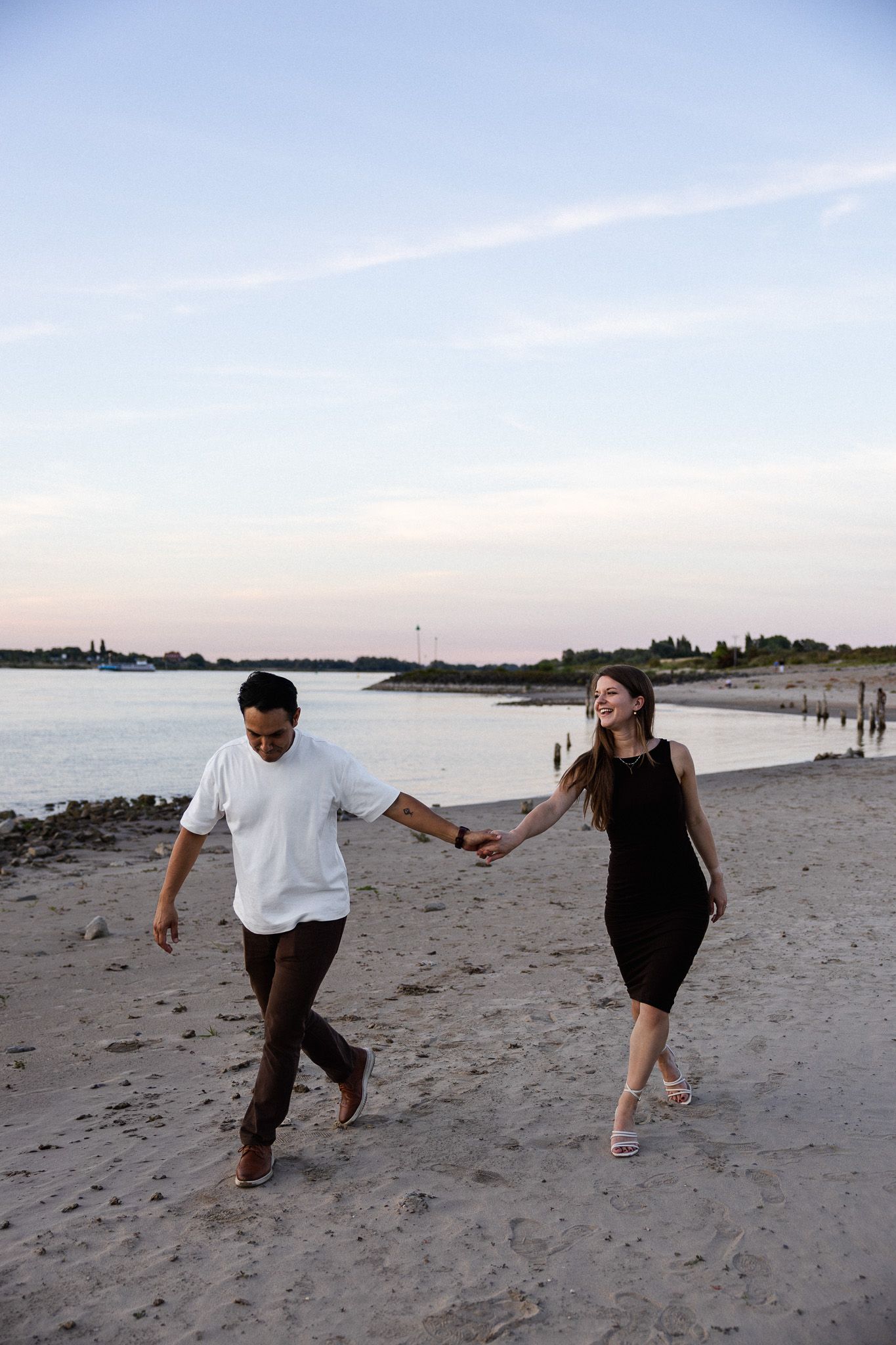 Spontane pre-wedding shoot op het Waalstrand in Nijmegen; aanstaand bruidspaar rent hand in hand langs het water tijdens de schemering