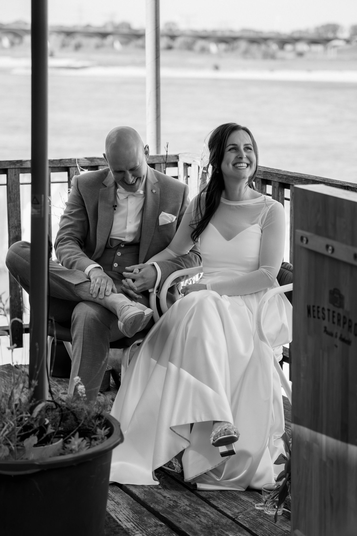 Sfeervol moment op het terras van de Meesterproef: bruid en bruidegom kijken lachend naar de spreker tijdens hun ceremonie in Nijmegen