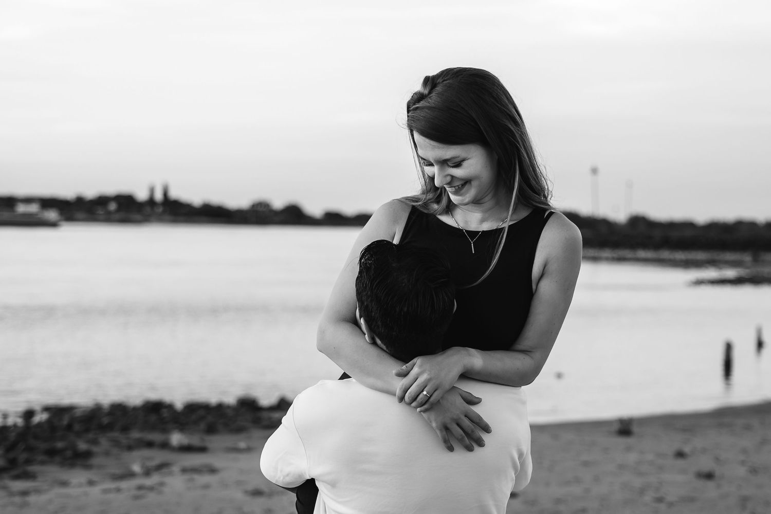 Black and white photo of a smiling woman holding a child on a sandy beach at dusk.