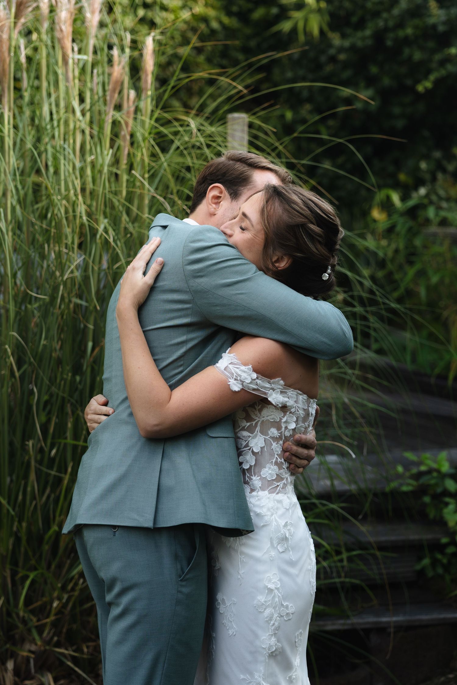 Bride and groom share an emotional embrace in a lush garden setting on their wedding day.