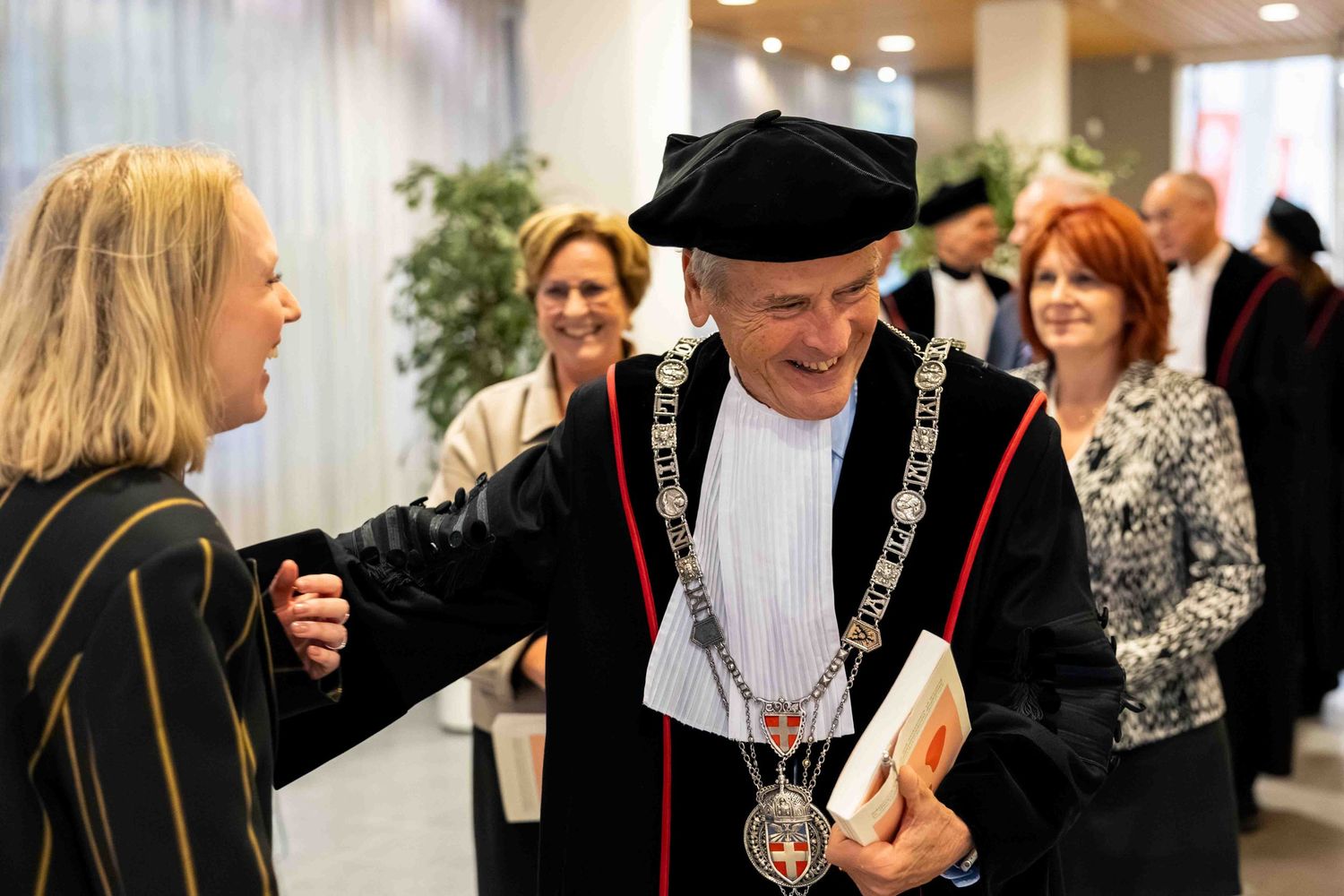 University rector in ceremonial robes and medallion greeting guests at an academic graduation ceremony.