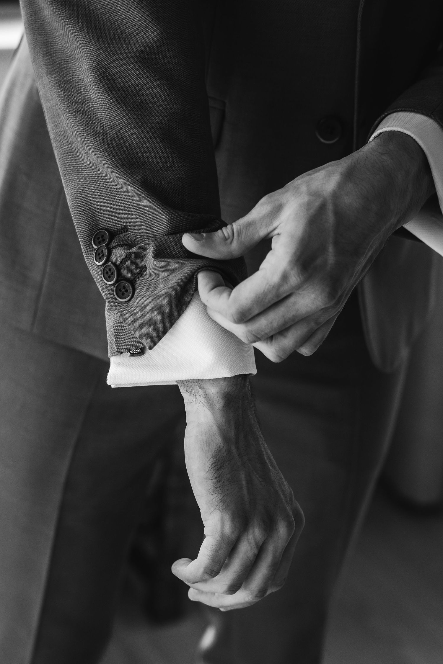 Close-up black and white photo of a groom adjusting his suit cuff and shirt sleeve before wedding ceremony.