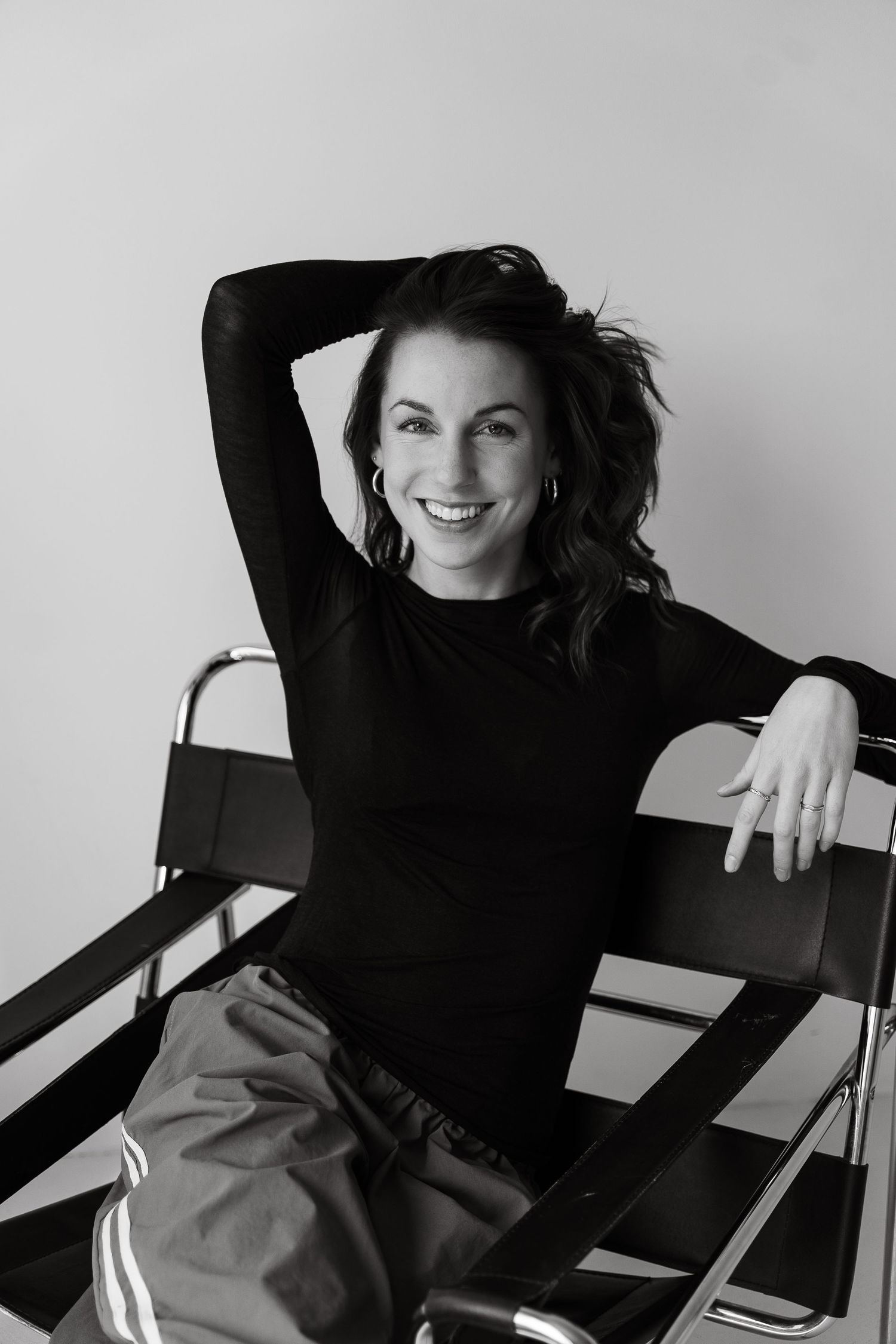 Black and white portrait of a smiling brunette woman in a black top, seated relaxed on a modern chair.