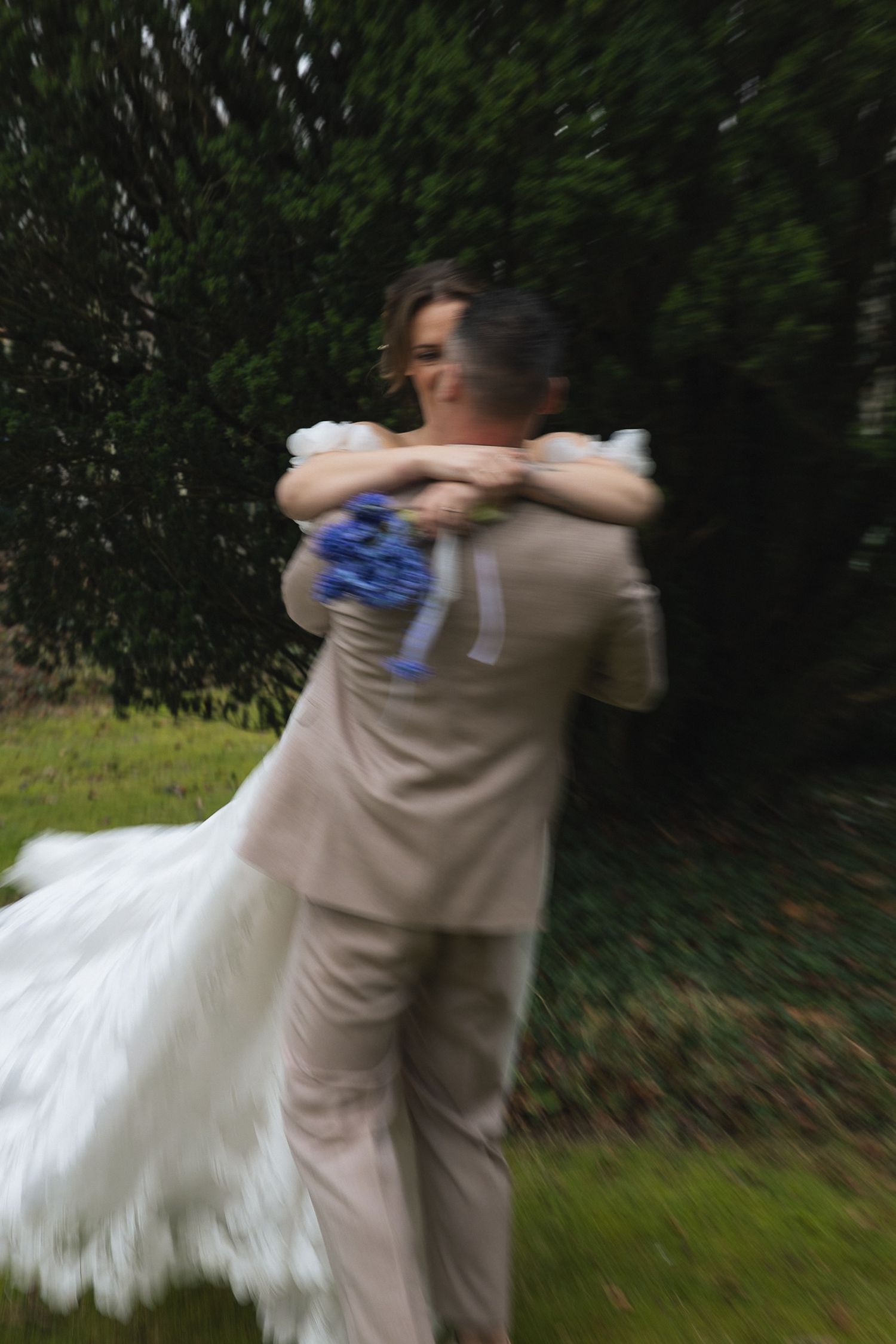Bride and groom share a joyful spinning embrace outdoors, with motion blur capturing their wedding day celebration.
