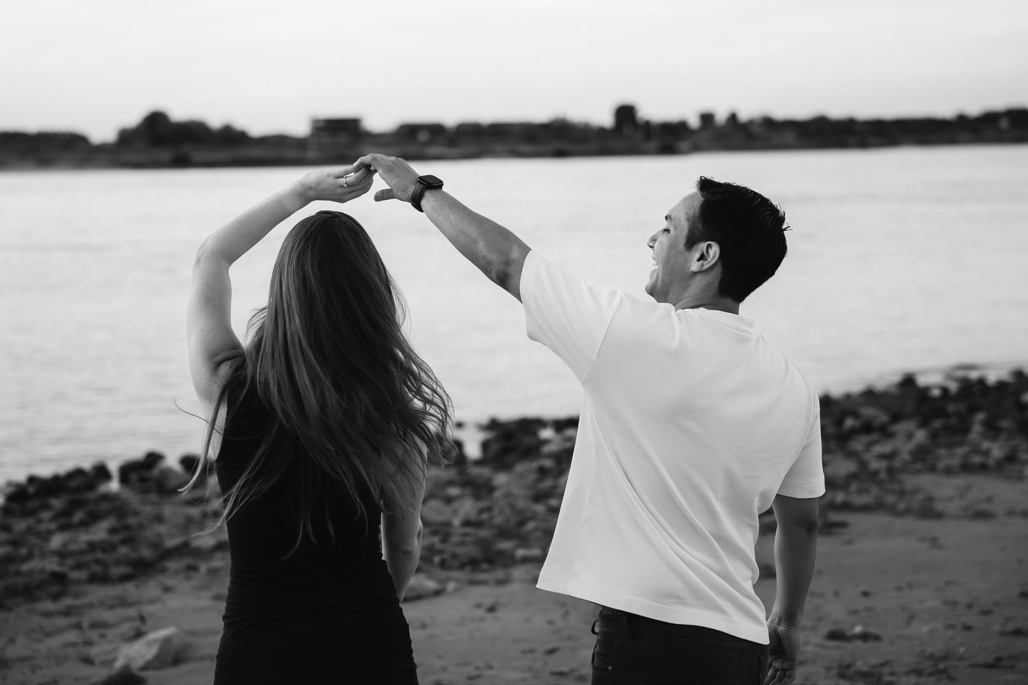Een koppel danst samen op het Waalstrand in Nijmegen nadat ze net verloofd zijn. Ongedwongen zwartwitfoto door trouwfotograaf atelier ROSA