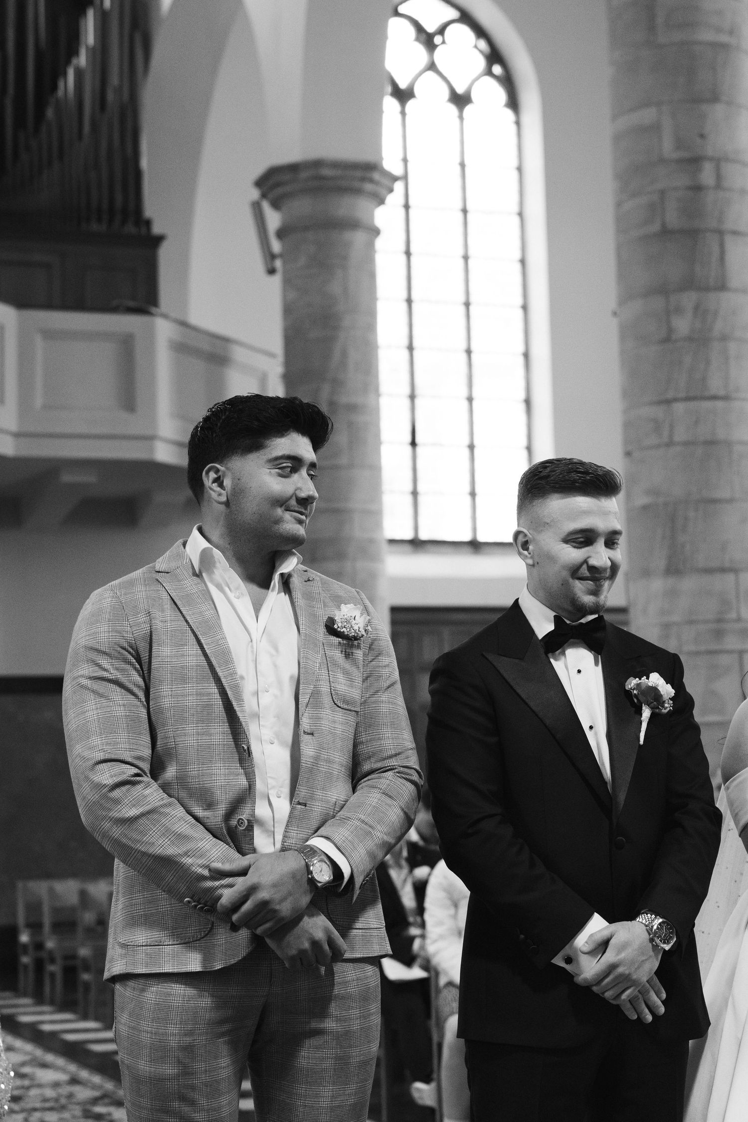 Two groomsmen in suits smiling at a church wedding ceremony, black and white photo.