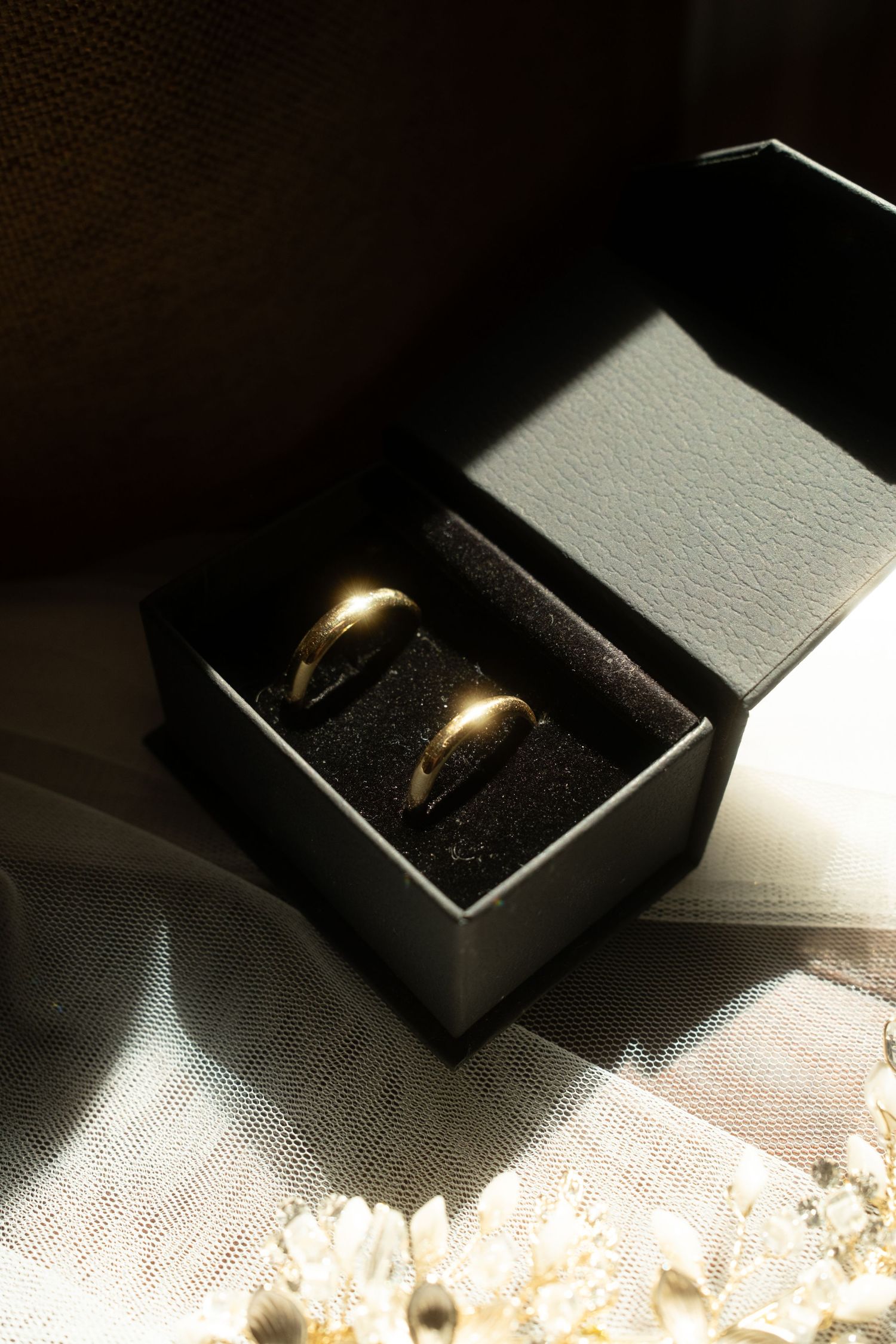 Two gold wedding bands displayed in an open black jewelry box on white lace fabric.